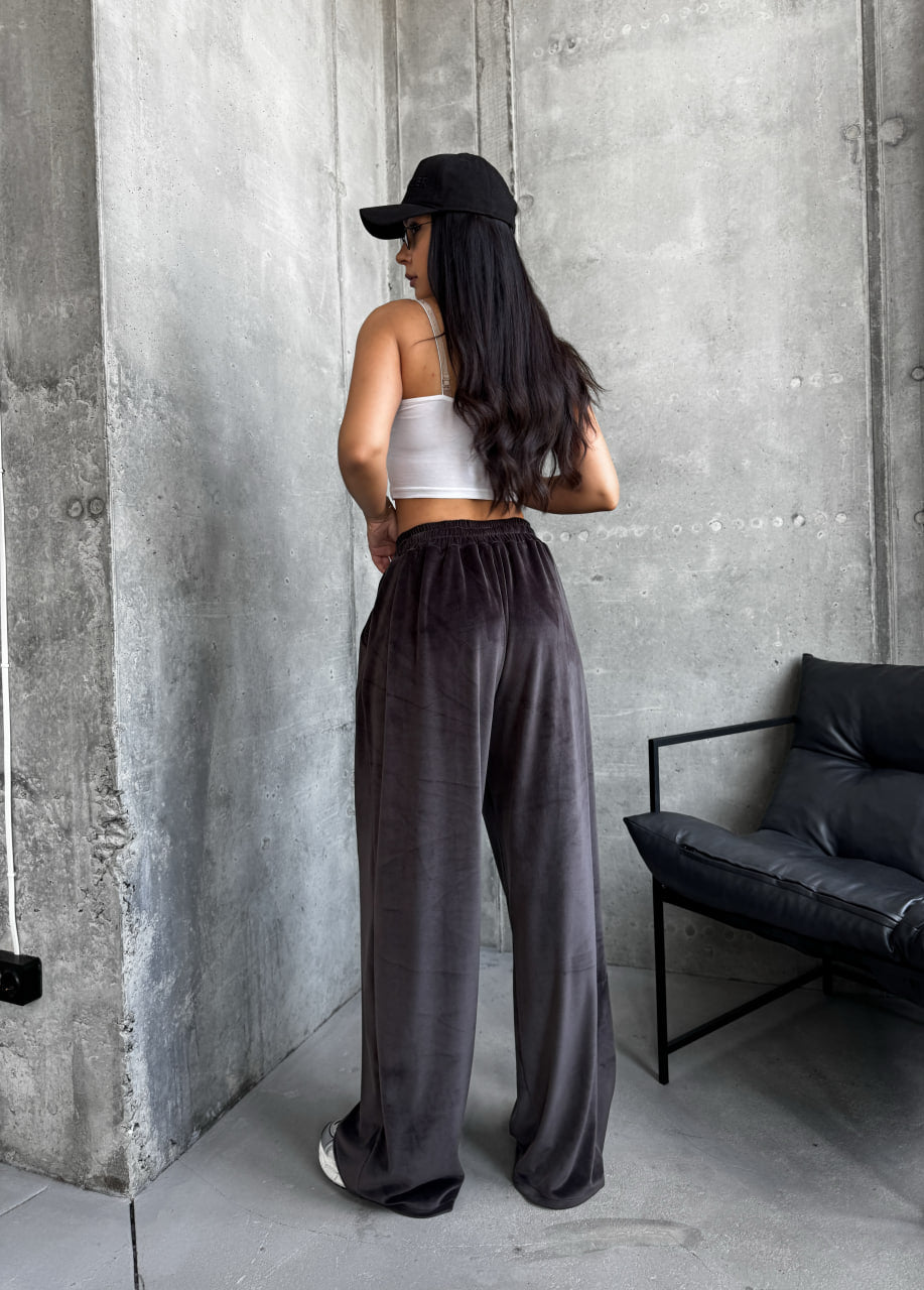 Woman wearing a white top and dark pants standing against a concrete wall.