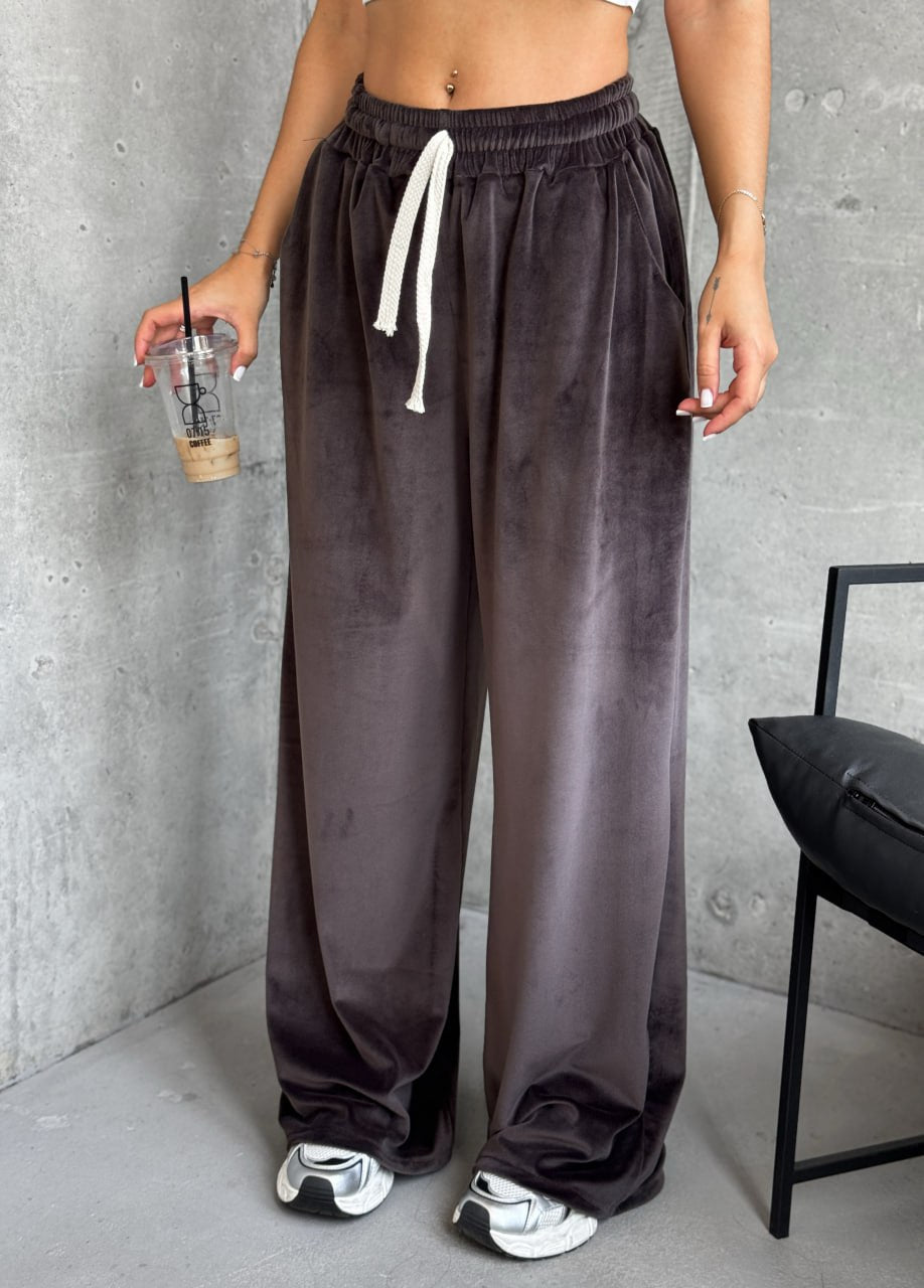 Person wearing brown wide-leg pants with a gray wall and chair in the background