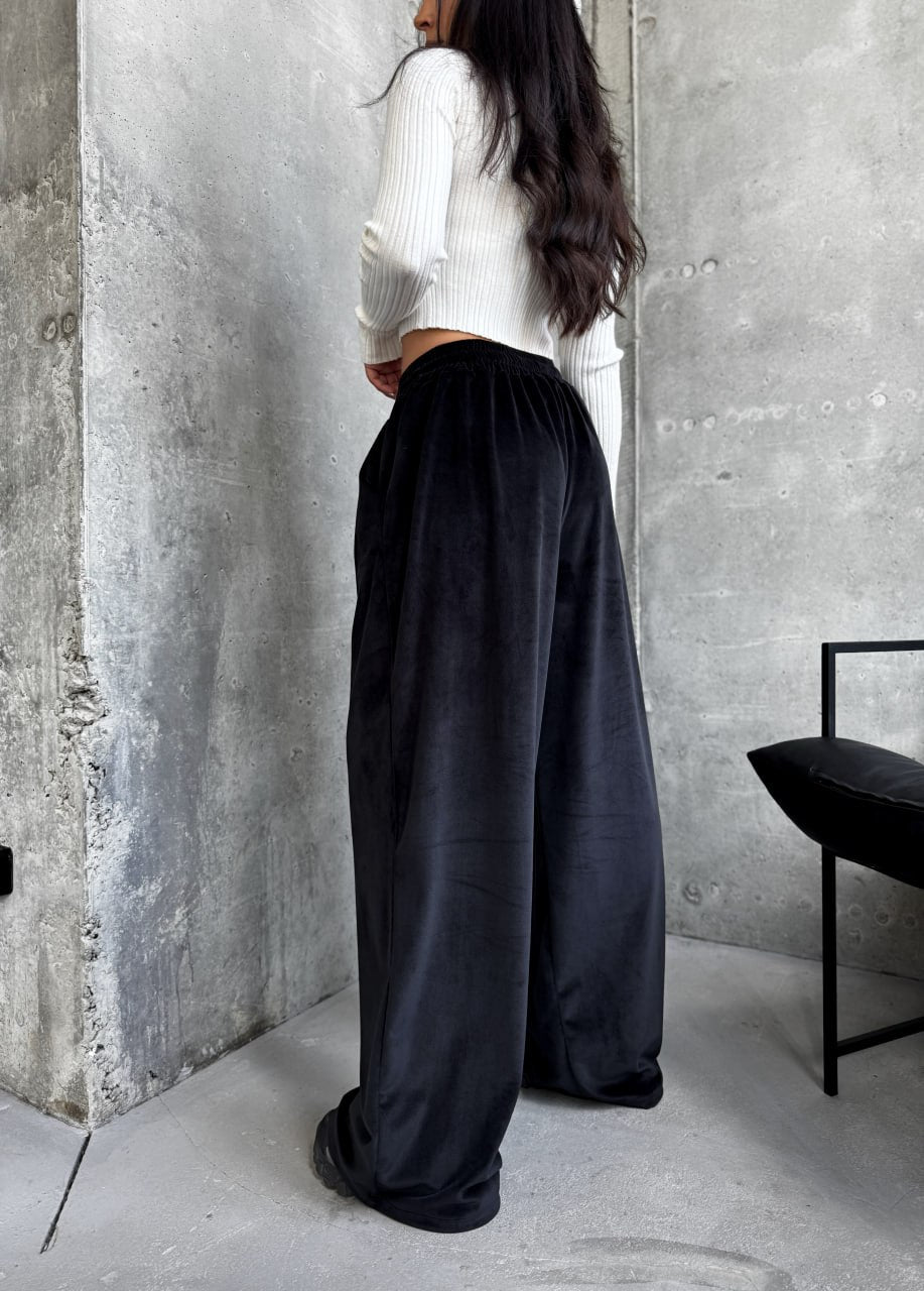 Person wearing a white top and black wide-leg pants standing against a concrete wall.
