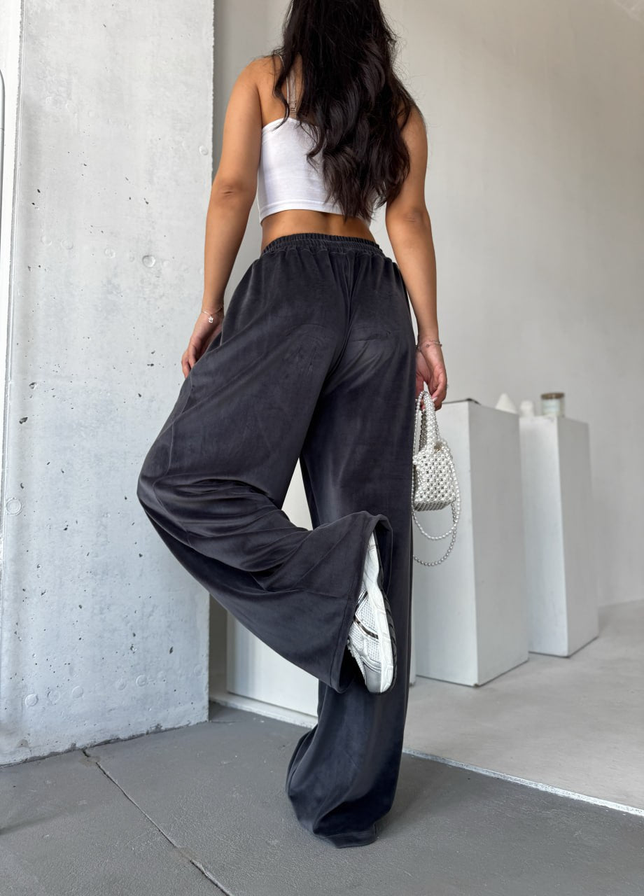 Person wearing dark gray wide-leg pants and a white top in an indoor setting.