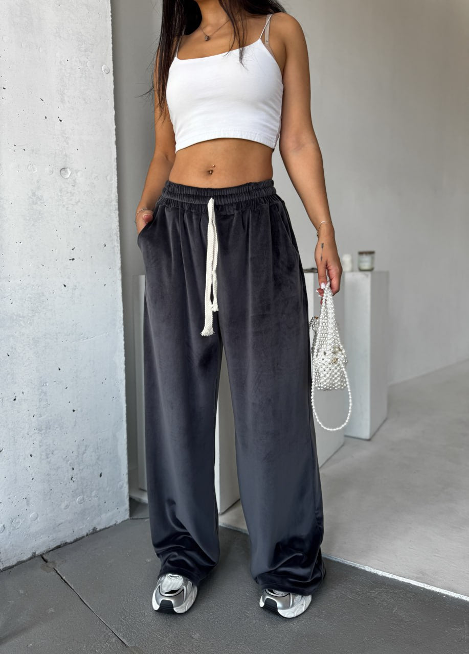 Person wearing a white crop top and dark gray sweatpants standing against a plain wall.
