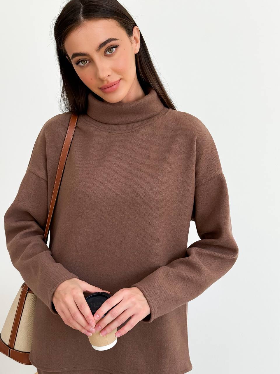 Woman wearing a brown sweater holding a coffee cup against a white background