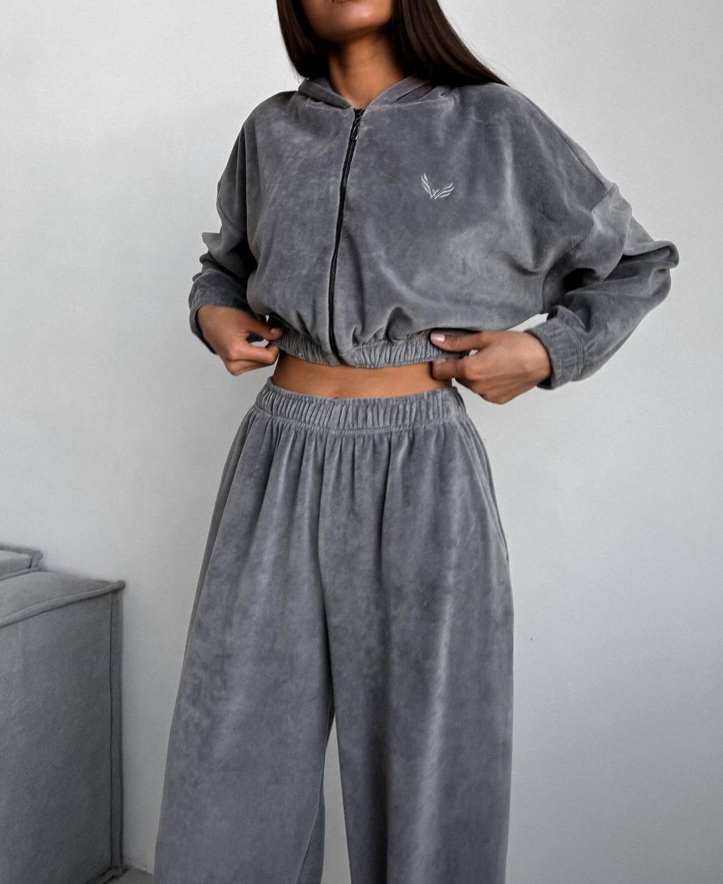 Person wearing a gray velour tracksuit with a small logo on a plain background