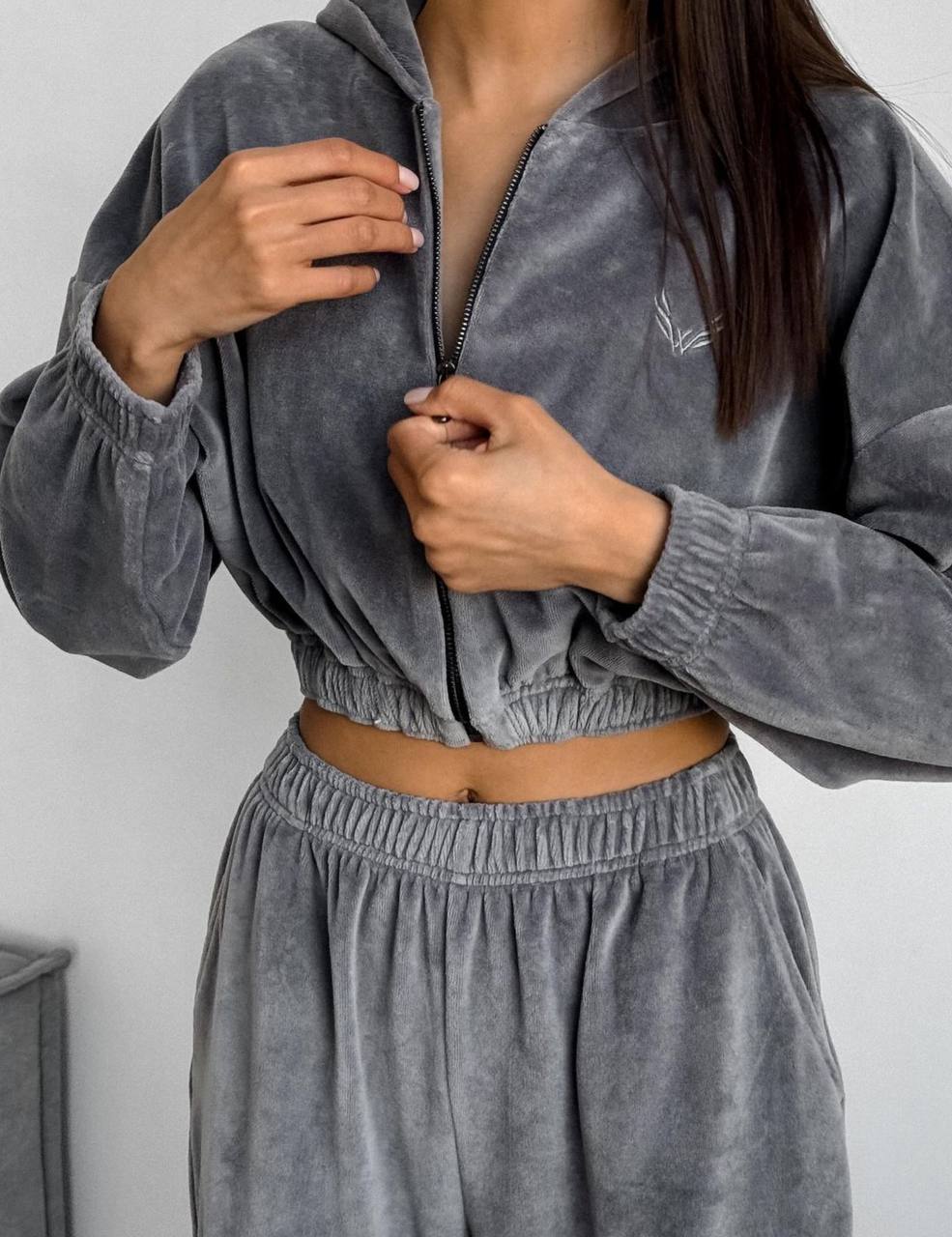 Person wearing a gray velour tracksuit against a plain background