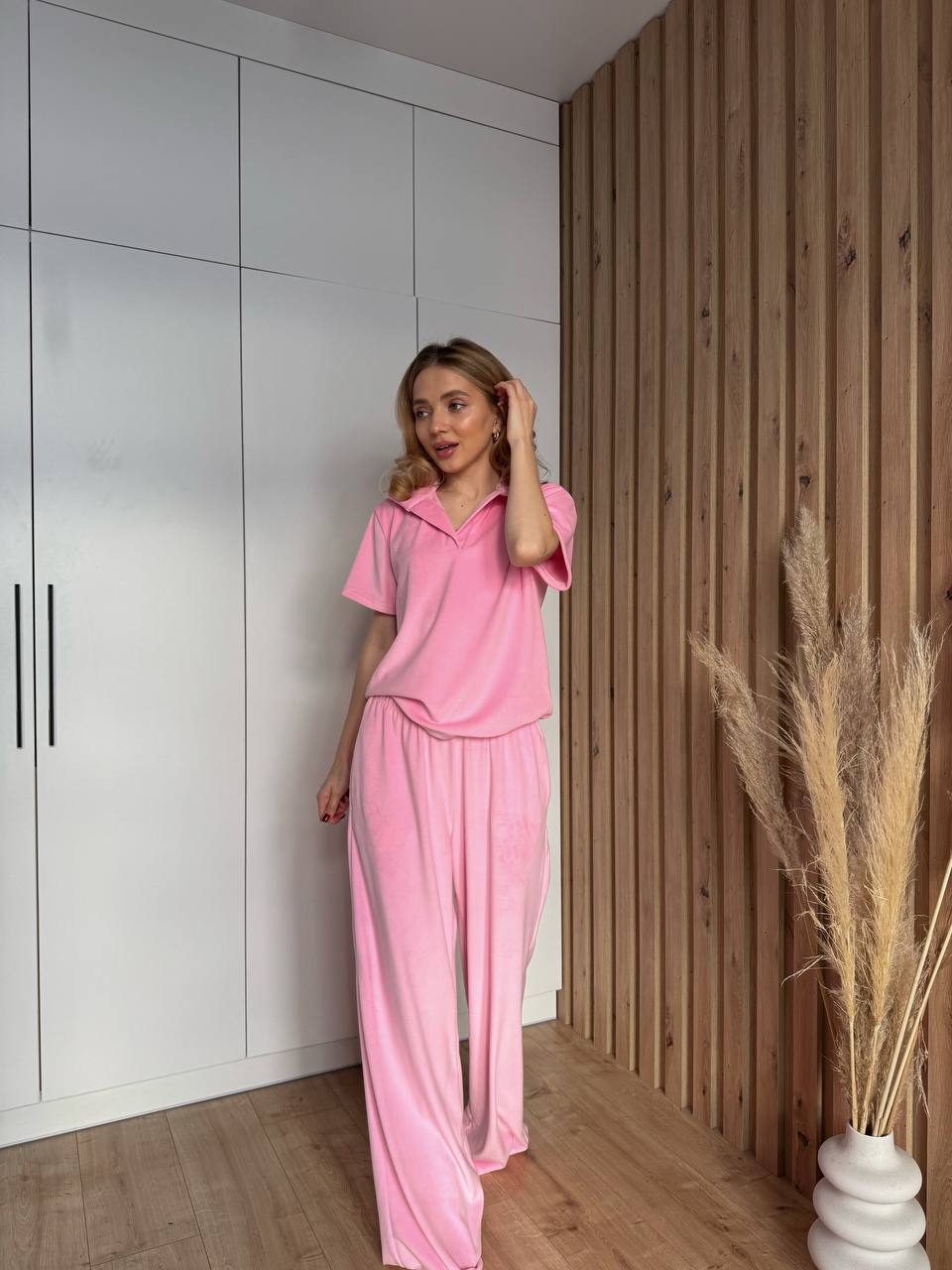 Woman in pink outfit standing in a room with white walls and wooden paneling.
