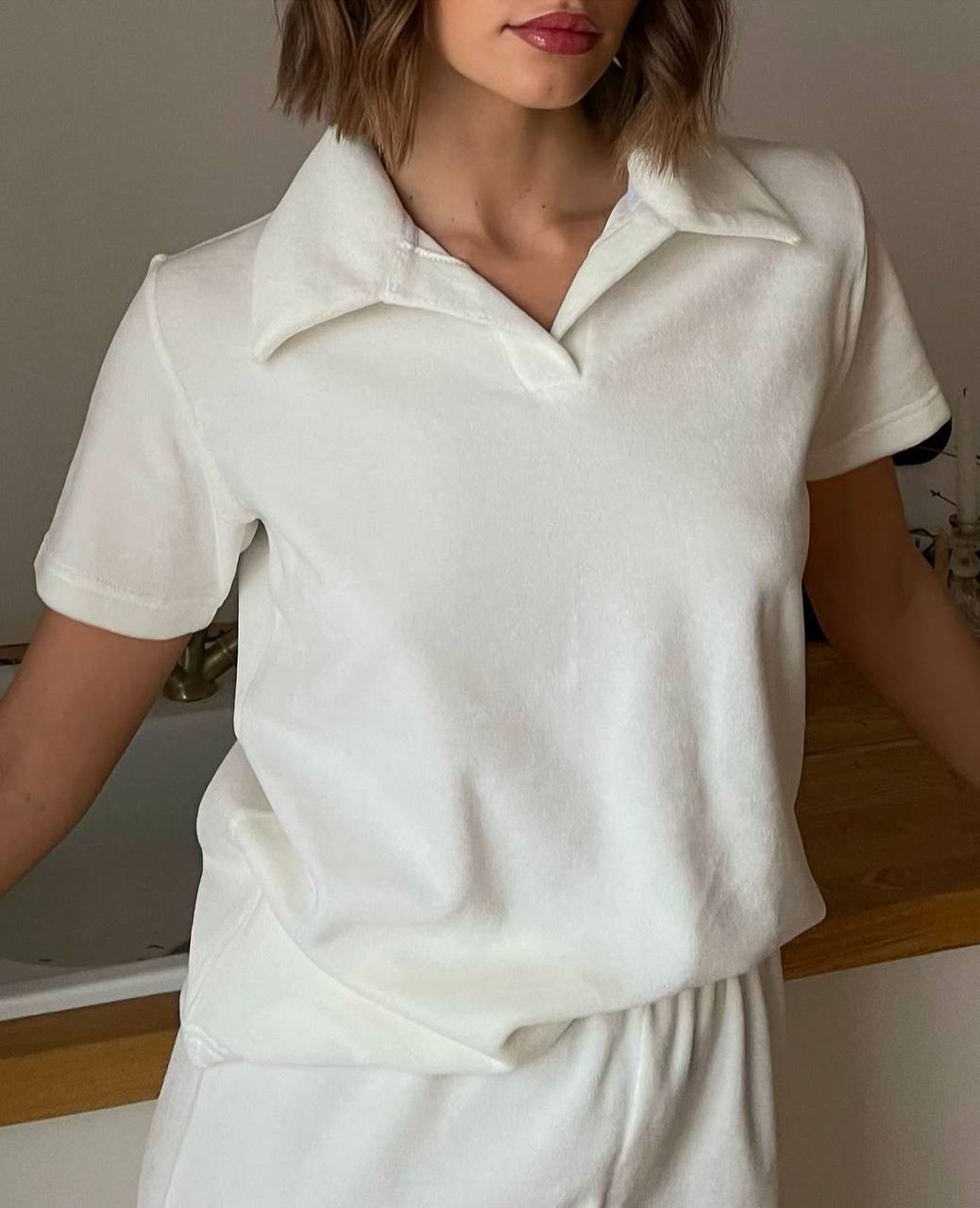 Person wearing a white polo shirt and pants indoors.