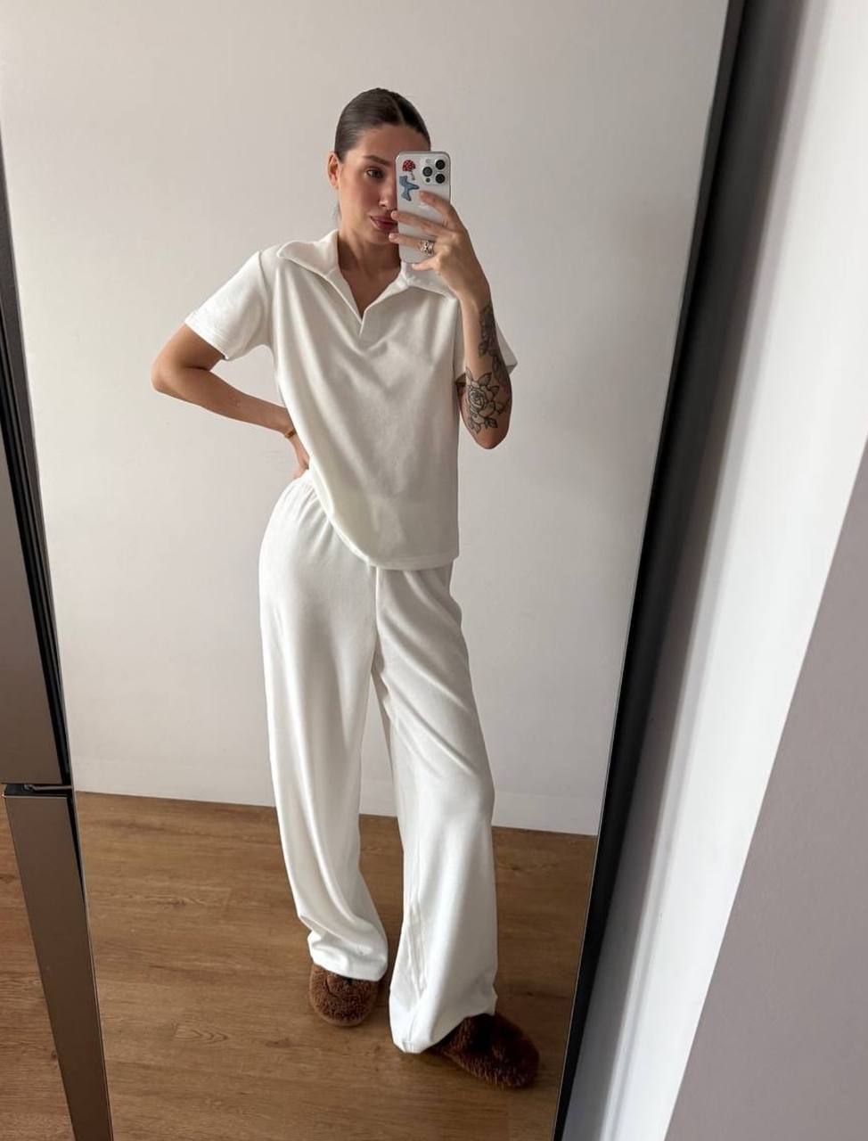 Person wearing a white outfit taking a mirror selfie in a minimalistic room.