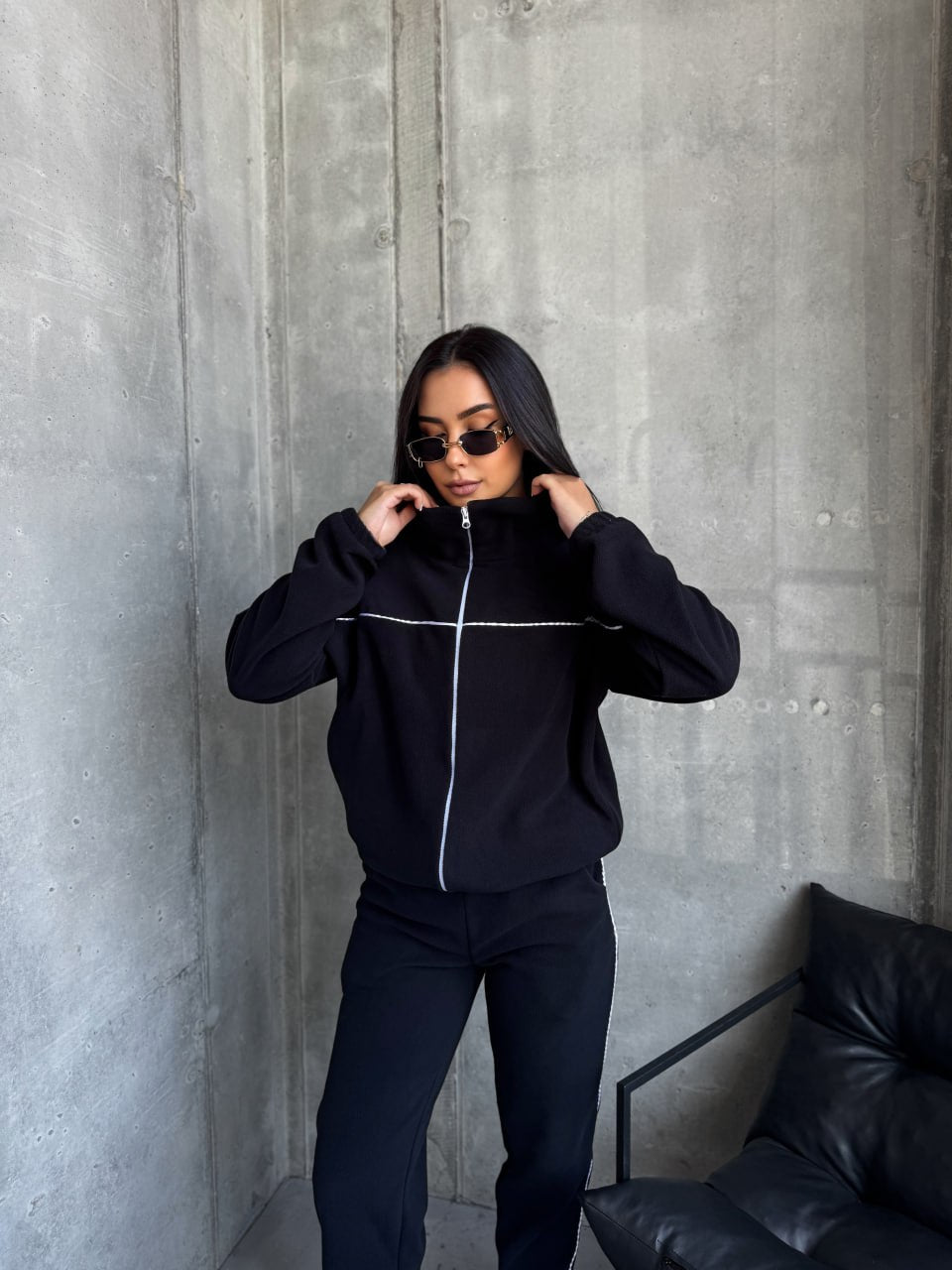 Person wearing a black tracksuit against a gray concrete wall.
