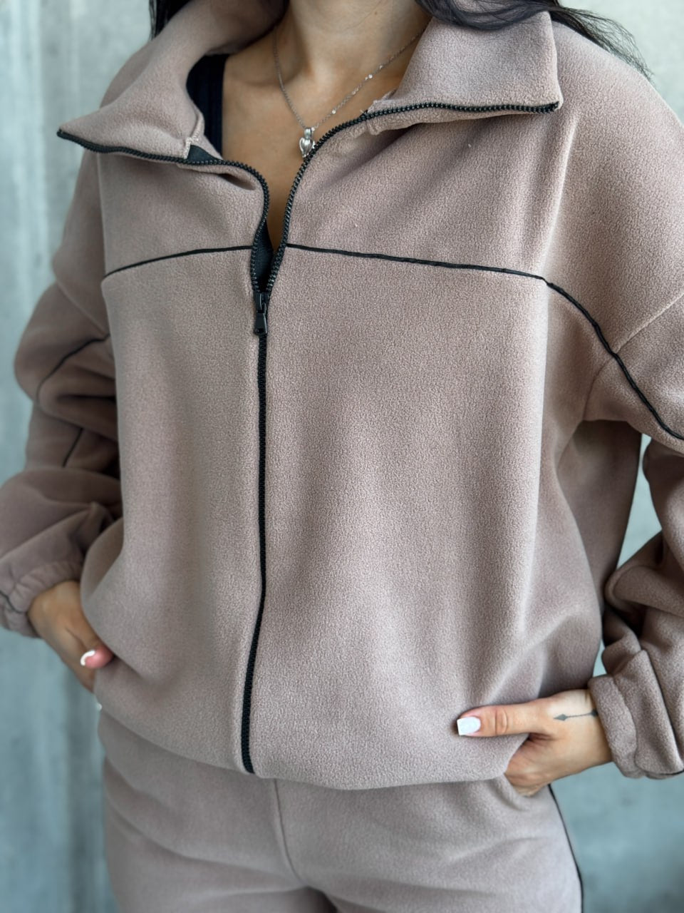Person wearing a beige tracksuit with black piping against a light blue background