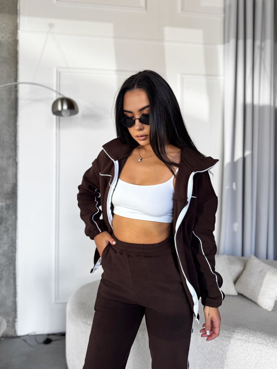 Woman wearing a brown jacket and pants with a white top in a modern room.