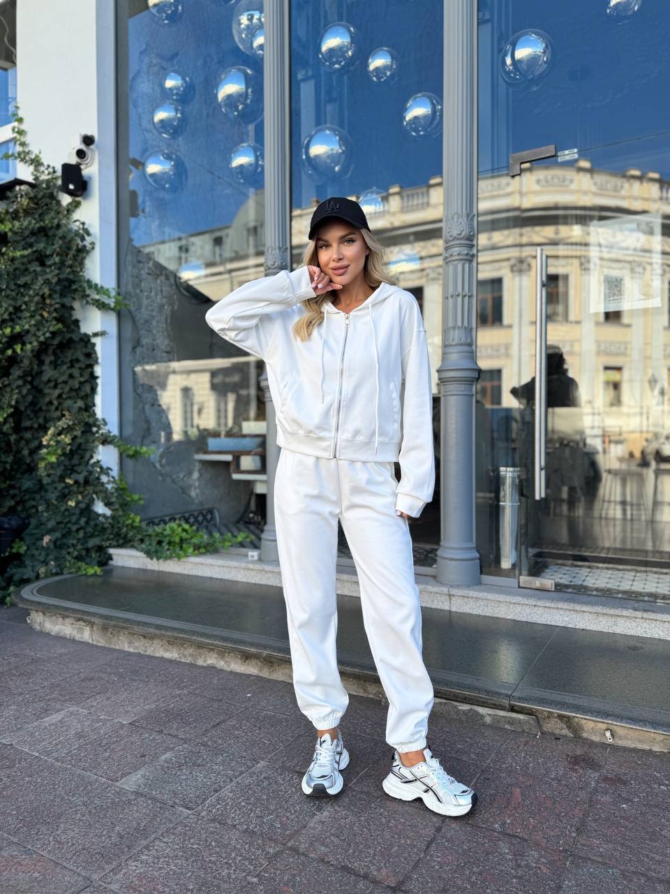 Person wearing a white tracksuit standing in front of a reflective glass building.