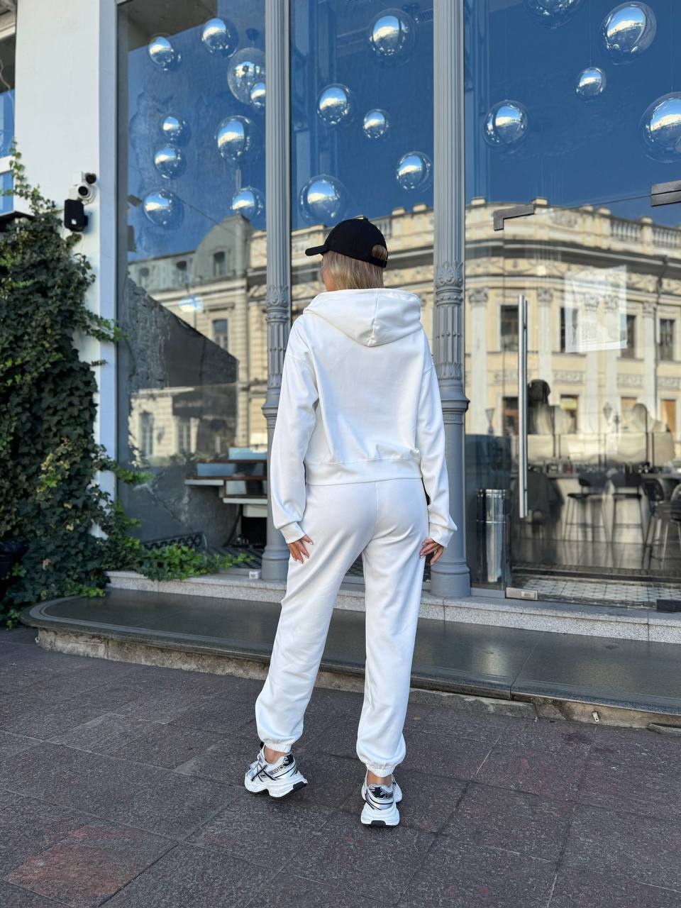 Person wearing a white tracksuit standing in front of a reflective building facade.