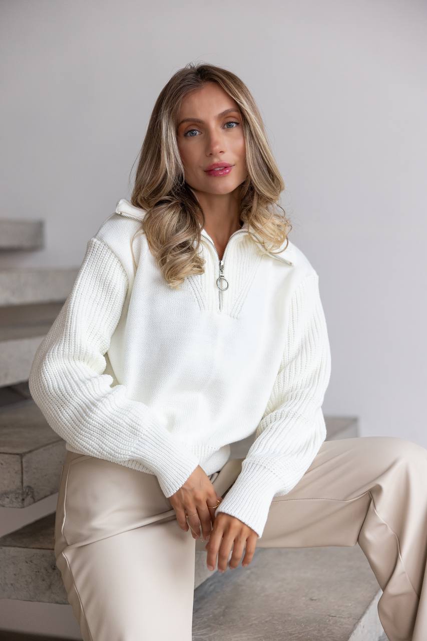 Woman wearing a white sweater and beige pants sitting on a staircase.