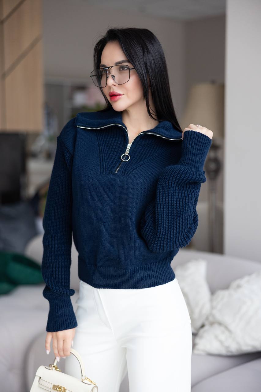 Woman wearing a navy blue sweater and white pants in an indoor setting