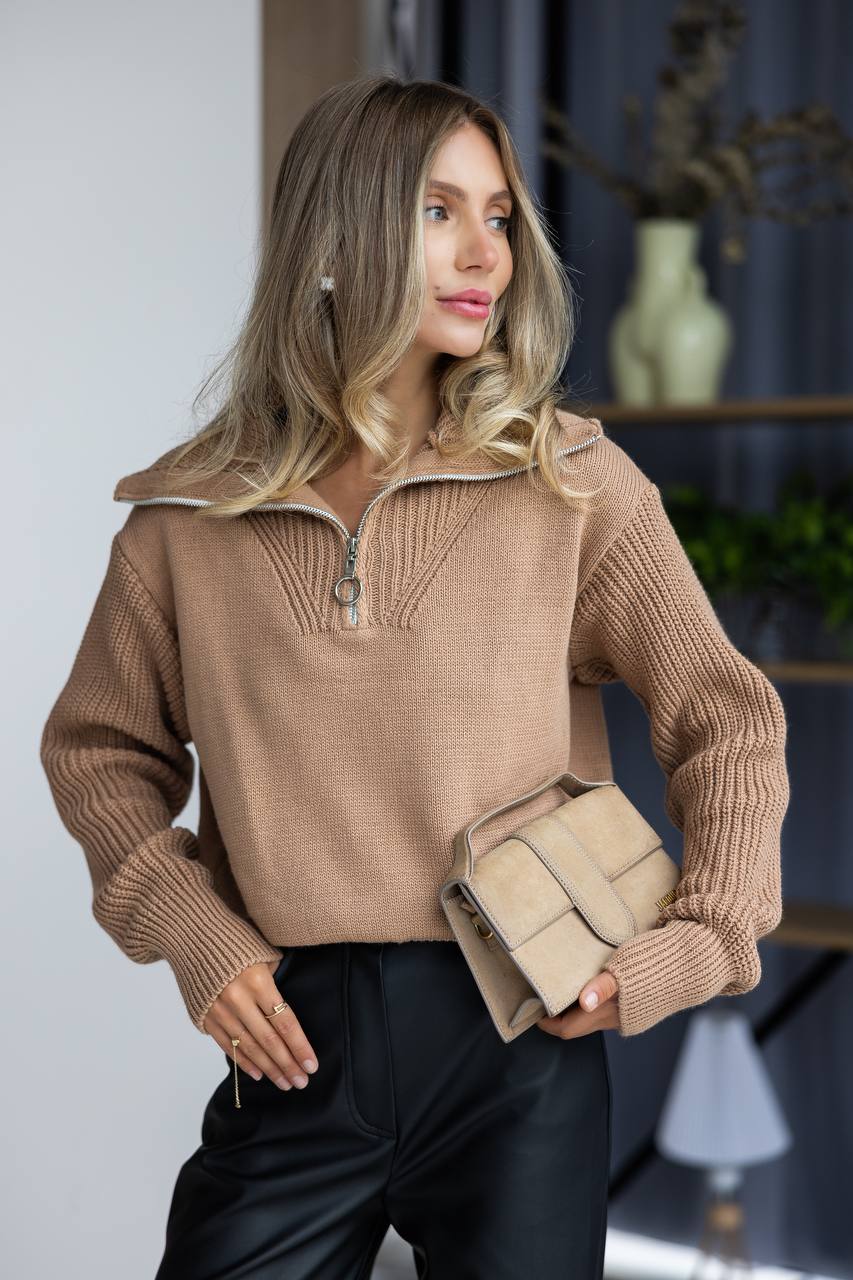 Woman wearing a brown ribbed sweater with a zipper, holding a beige clutch.