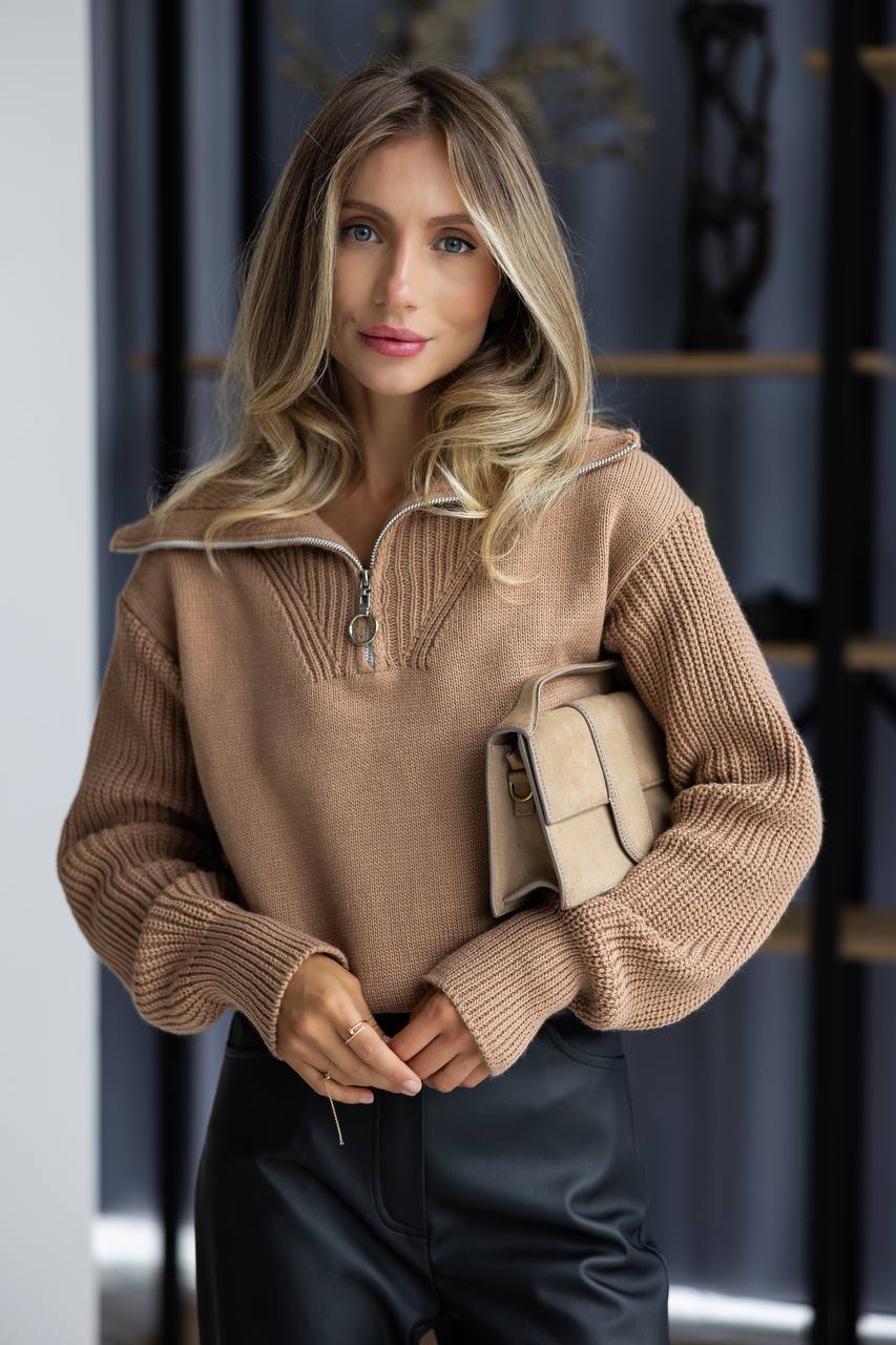 Woman wearing a brown sweater holding a beige handbag indoors.