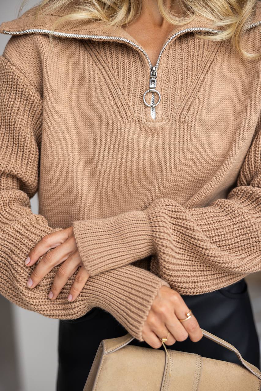 Close-up of a person wearing a beige knit sweater with a zipper.