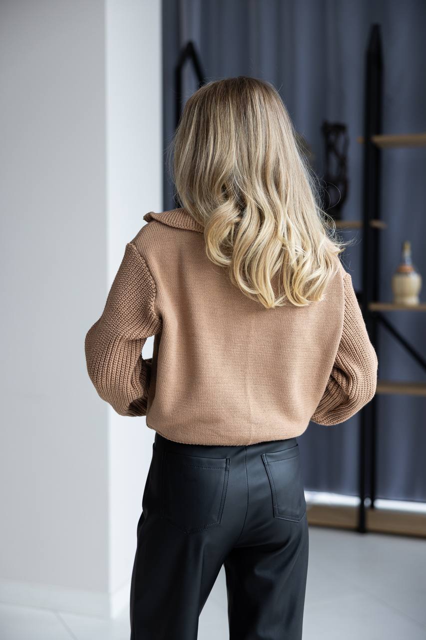 Person wearing a brown sweater and dark pants in an indoor setting