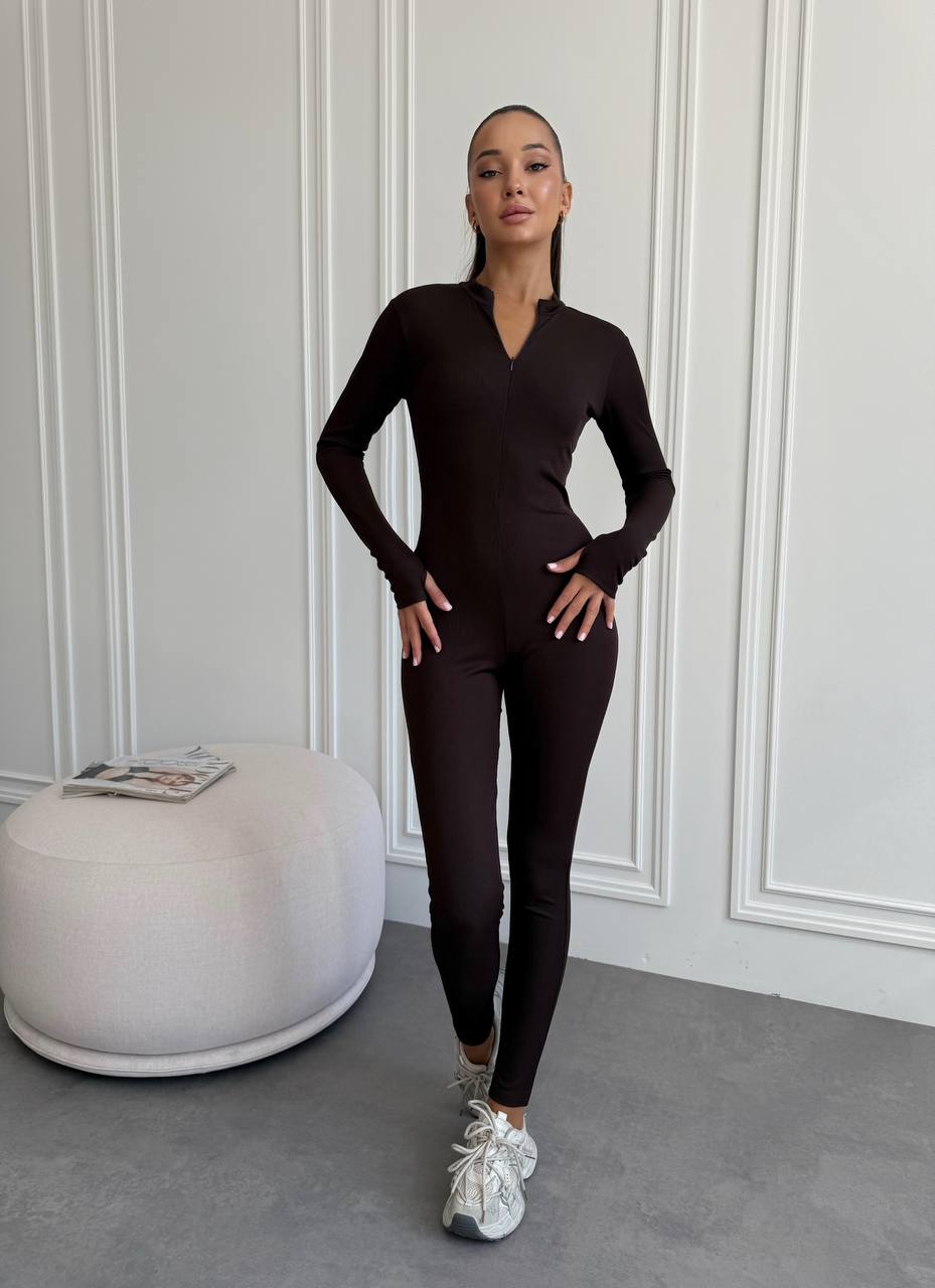 Person wearing a black outfit standing in a room with a white wall and gray floor.