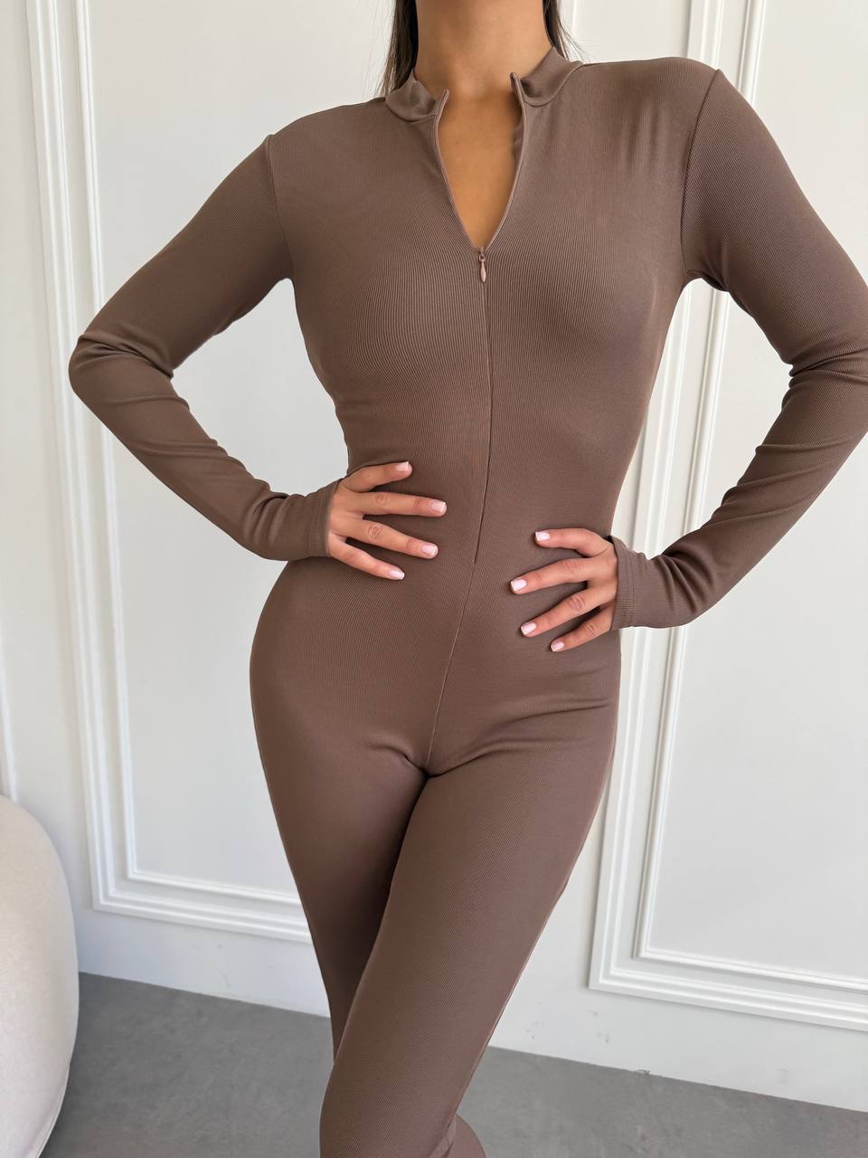 Person wearing a brown bodysuit against a white wall