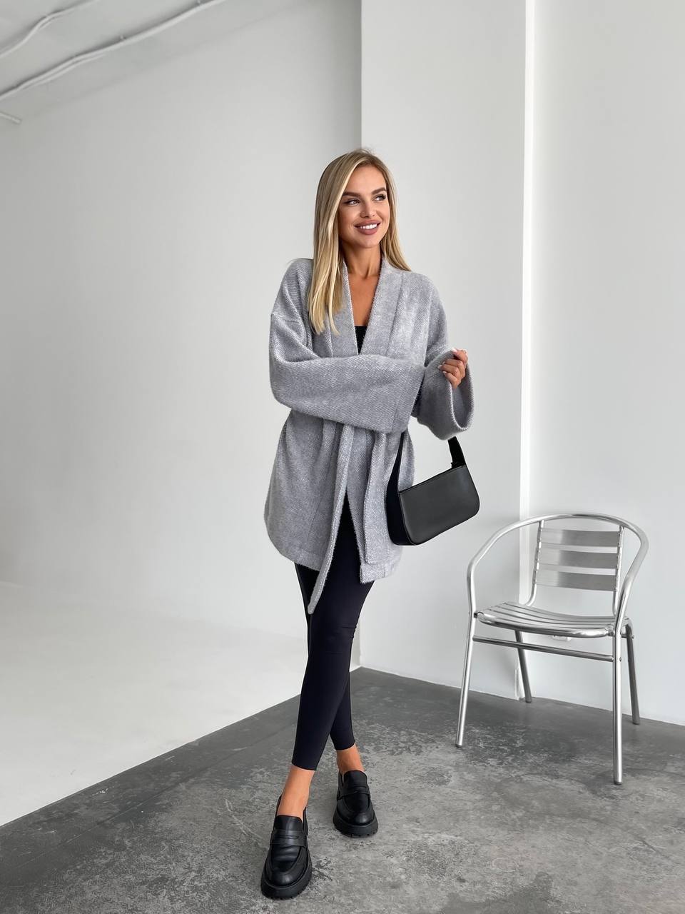 Woman wearing a gray cardigan, black leggings, and black shoes in an indoor setting.