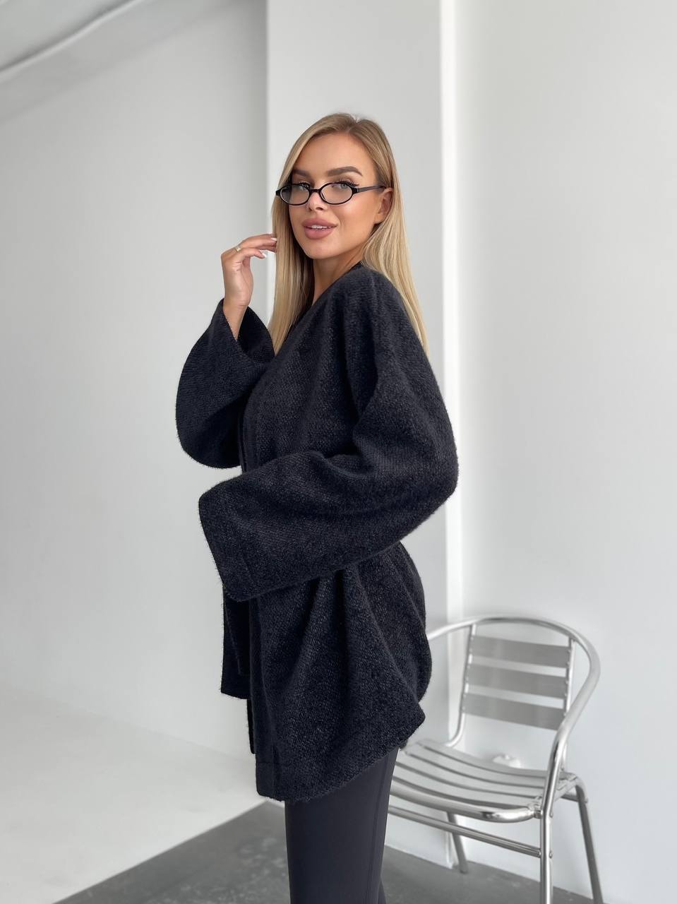 Woman wearing a dark gray oversized sweater in a minimal indoor setting.