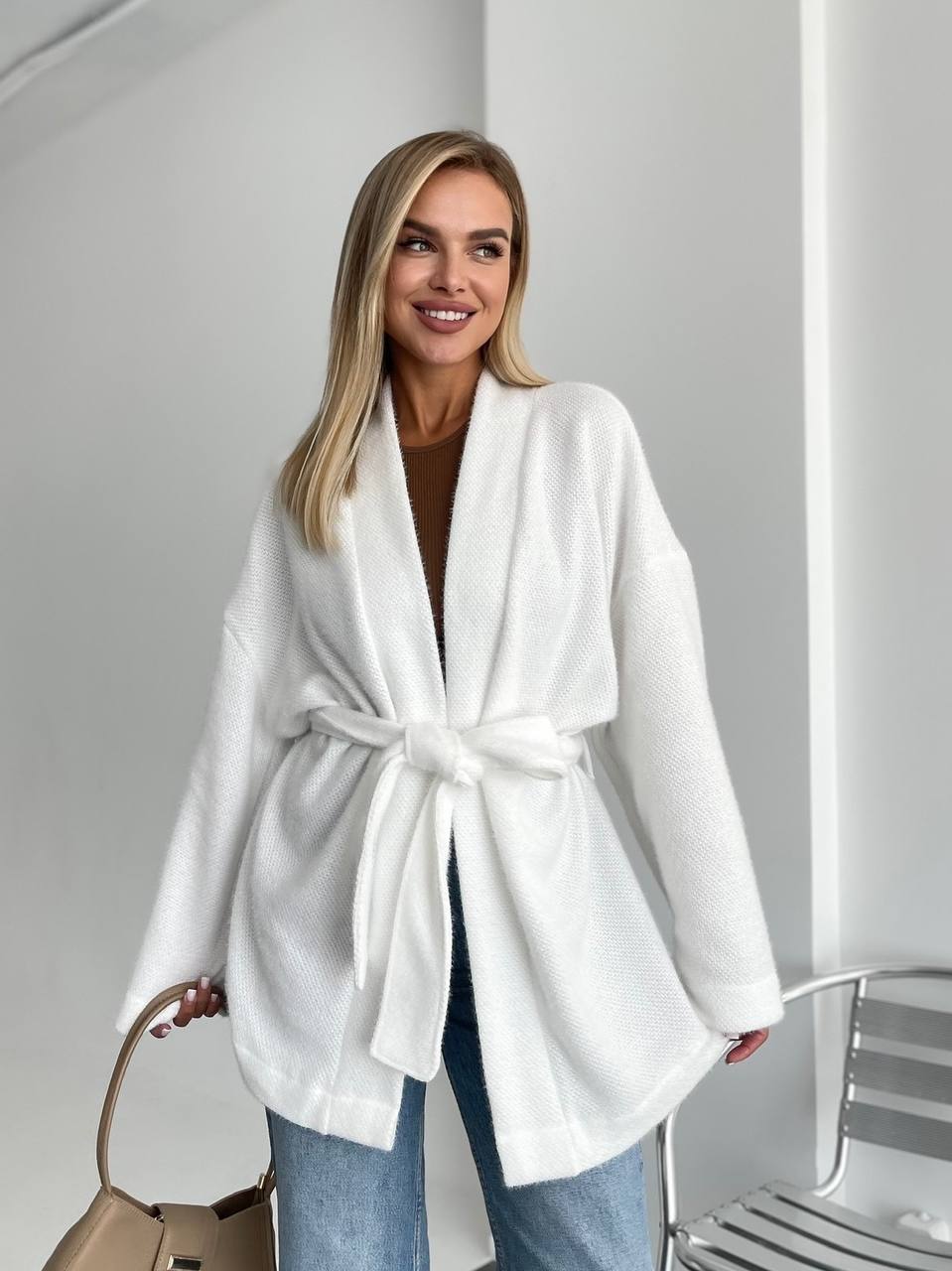 Woman wearing a white belted coat with a plain background