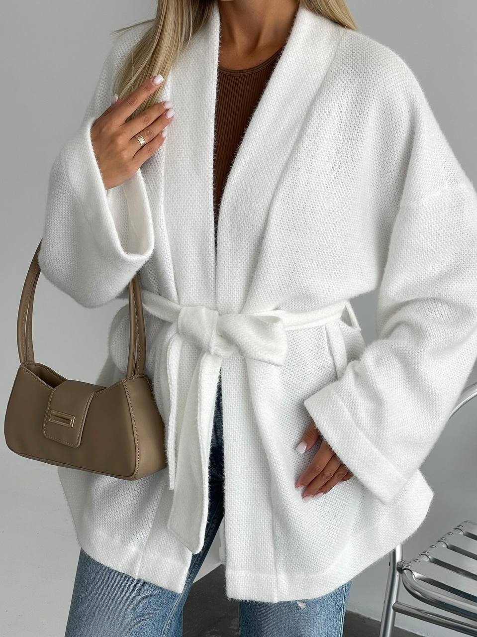 Person wearing a white robe with a brown handbag on a gray background