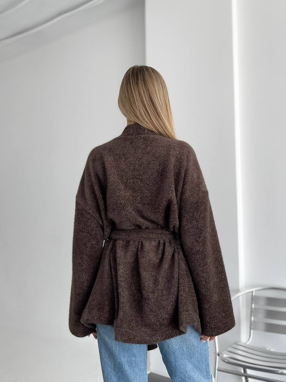 Person wearing a brown coat with a white wall background