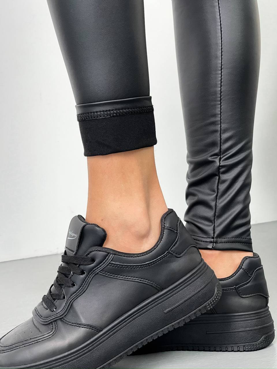 Black sneakers worn with black pants on a light gray background