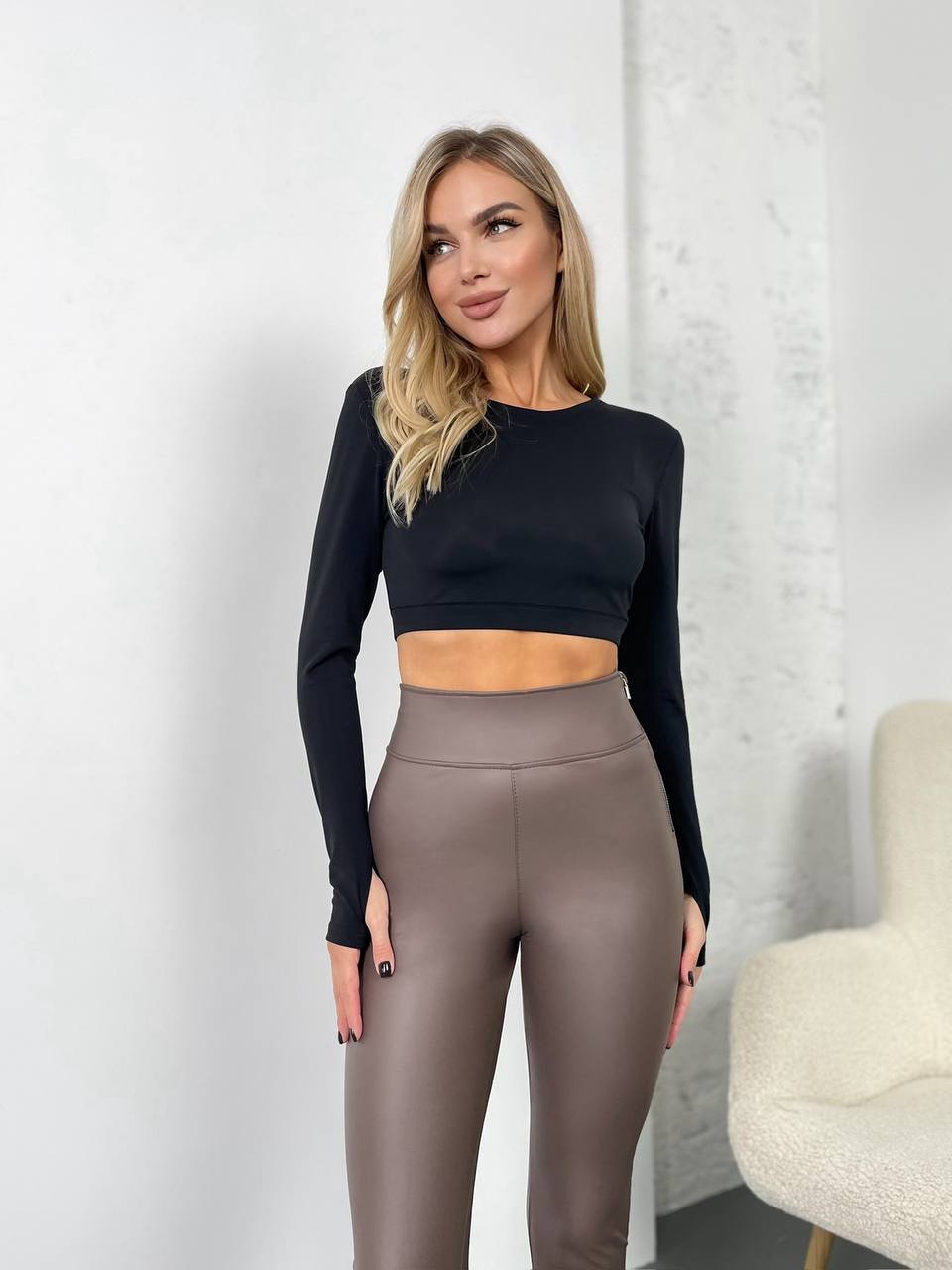 Woman wearing a black long-sleeve top and brown leggings against a white background