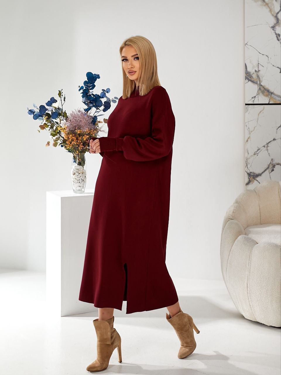 Woman in a burgundy dress holding flowers in a modern interior setting