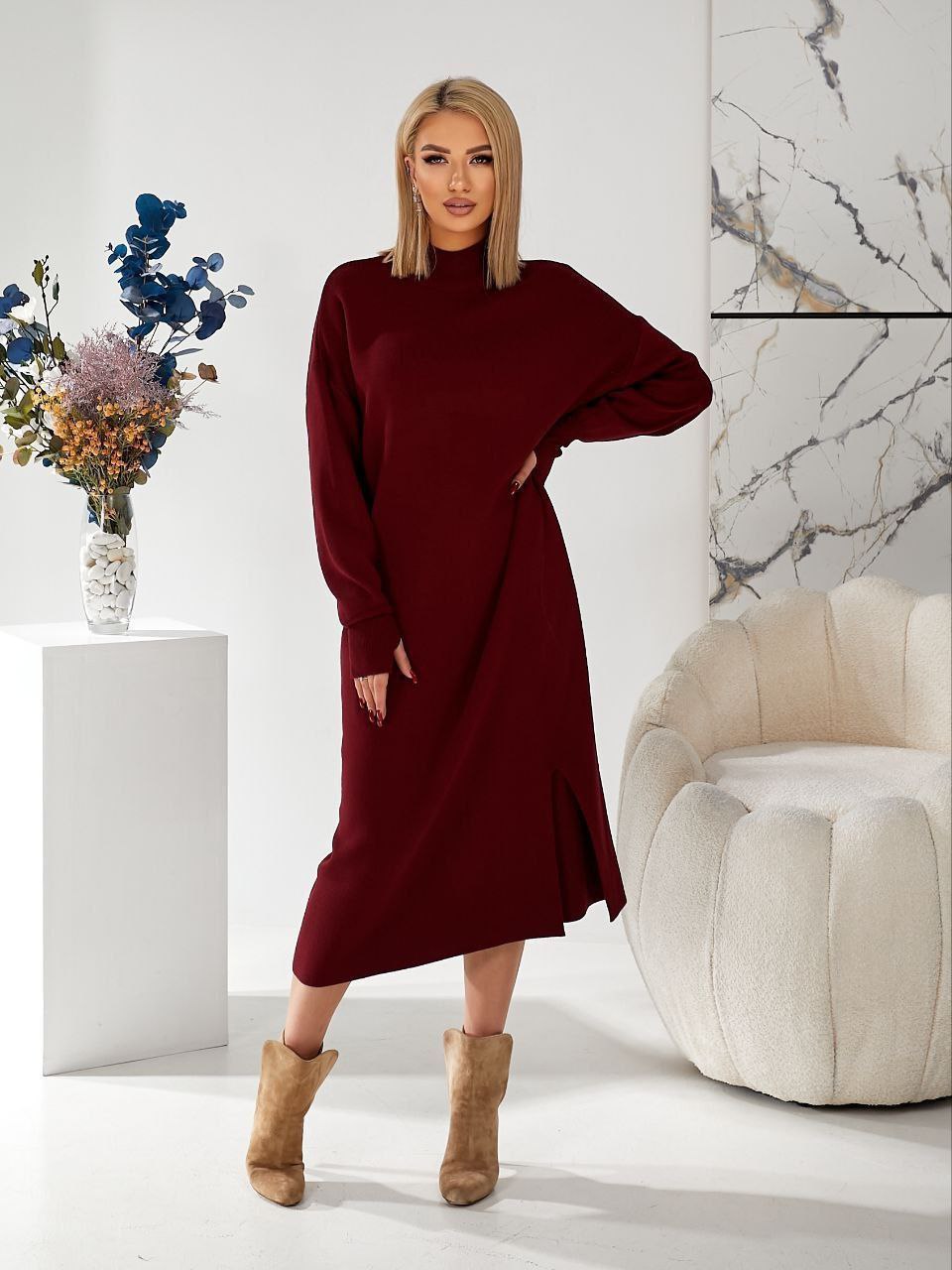 Woman wearing a burgundy dress with long sleeves in a modern interior setting.