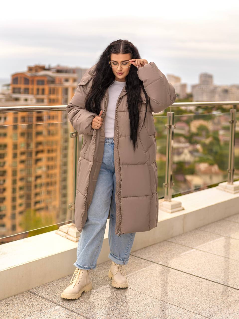 Woman wearing a long brown puffer coat on a rooftop with cityscape background