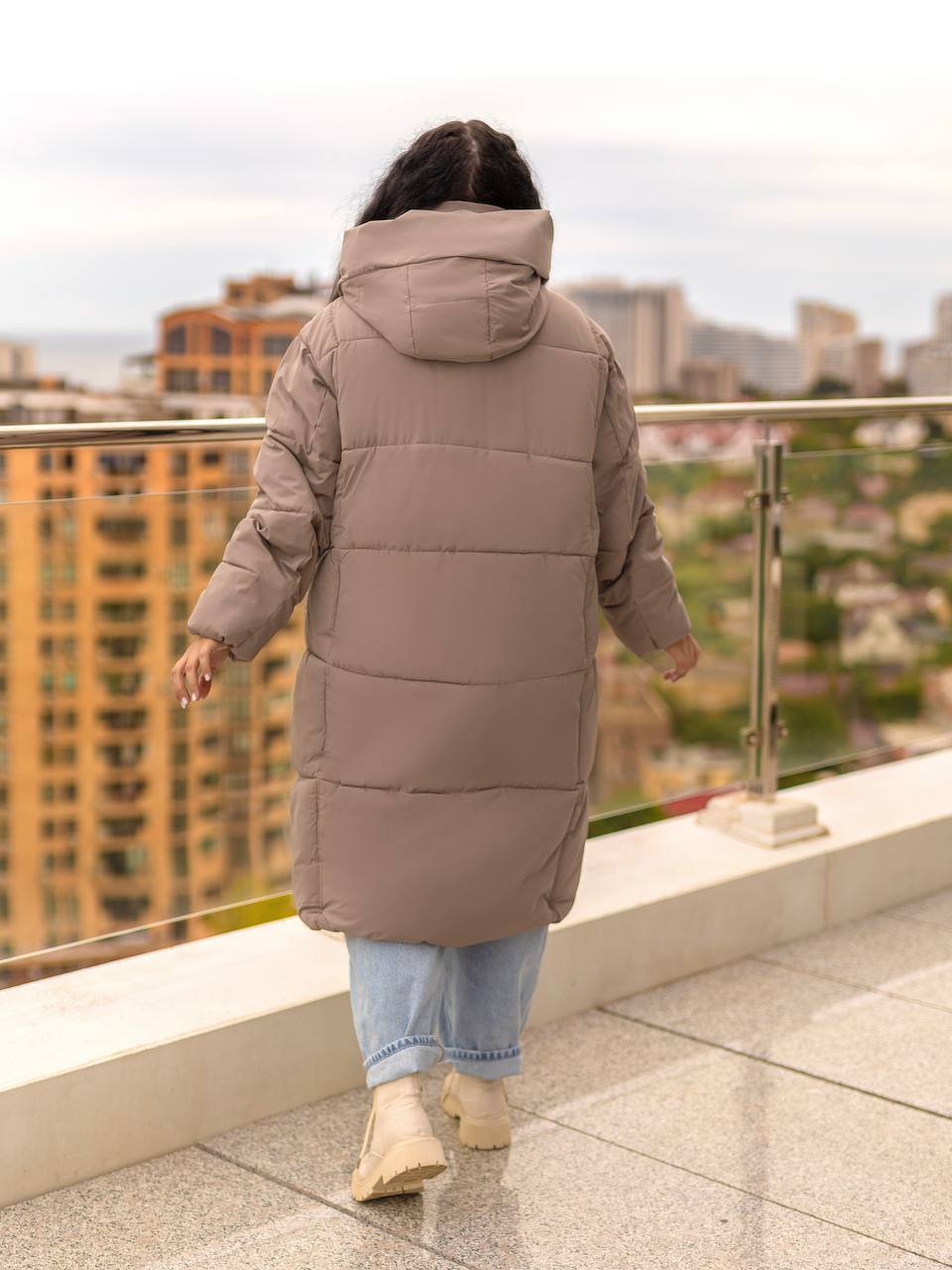 Person wearing a long beige puffer coat on a rooftop with cityscape in the background