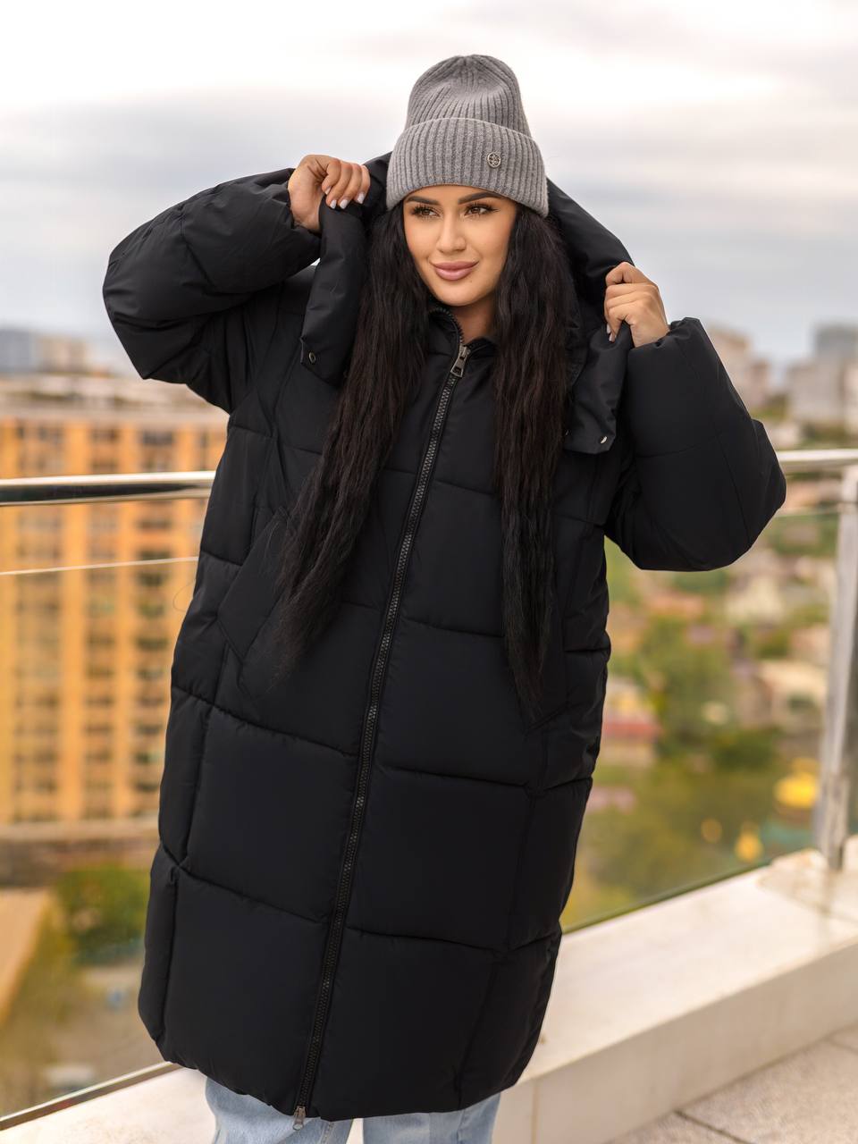 Person wearing a black puffer coat and gray beanie outdoors with buildings in the background