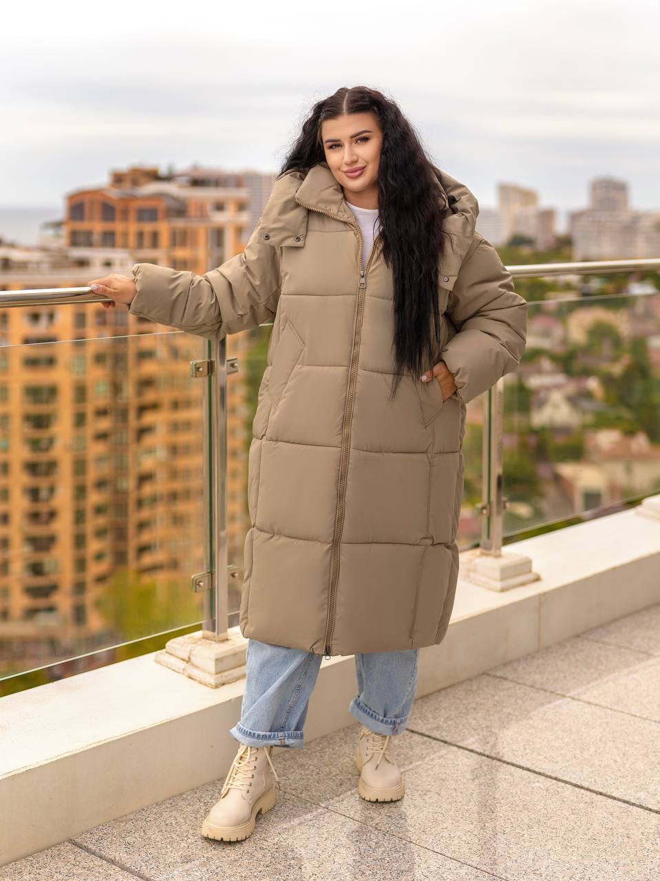 Woman wearing a long beige puffer coat on a rooftop with cityscape background