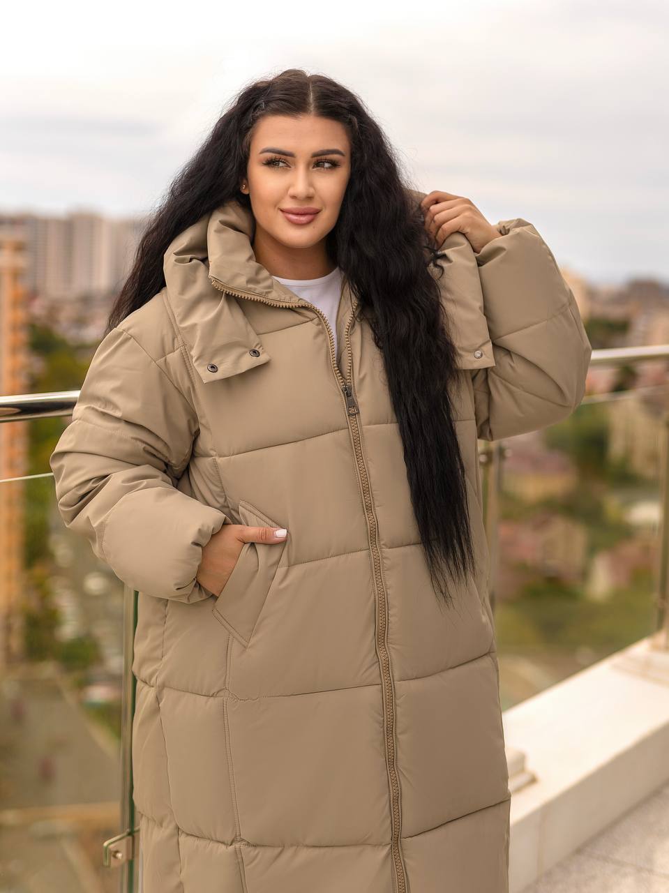 Woman wearing a beige puffer coat on a rooftop with a cityscape background