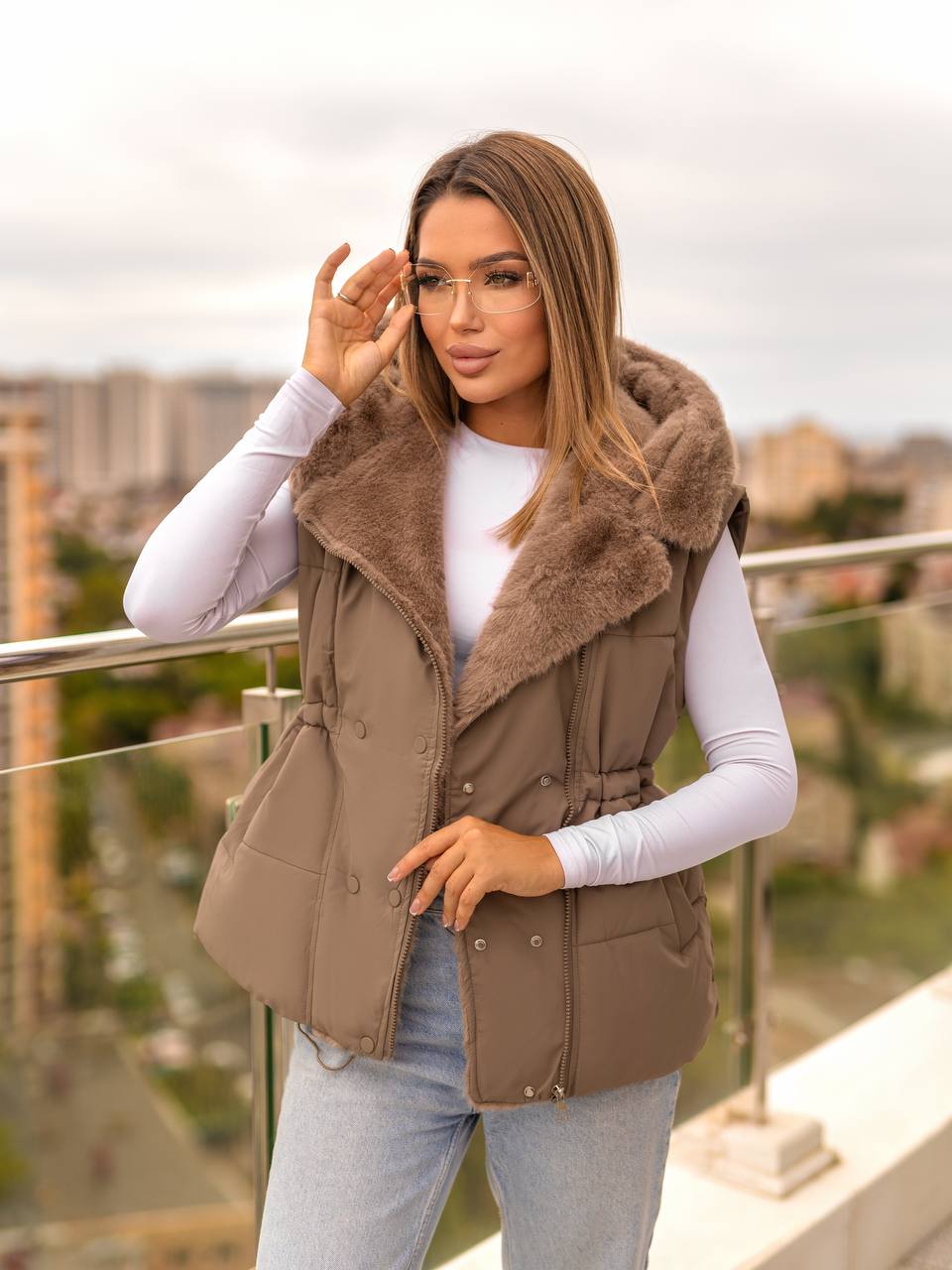 Woman wearing a brown vest with a cityscape in the background