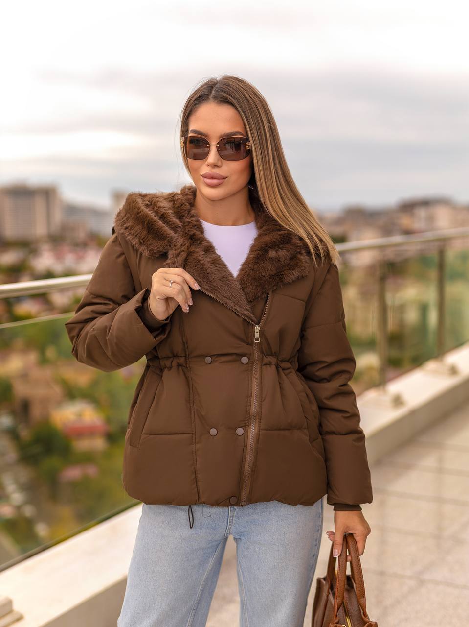 Woman wearing a brown puffer jacket with fur trim outdoors.