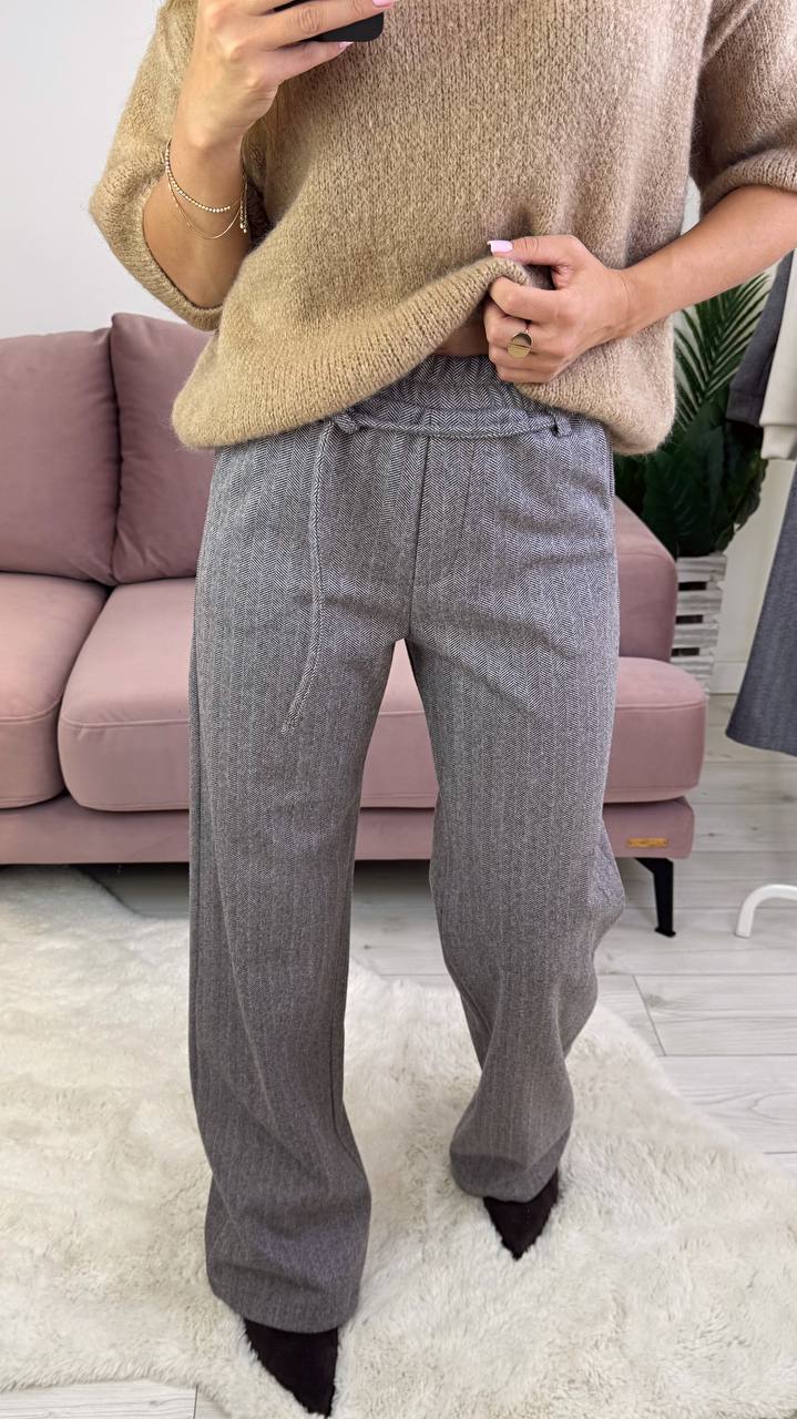 Person wearing a beige sweater and gray pants in a living room setting.