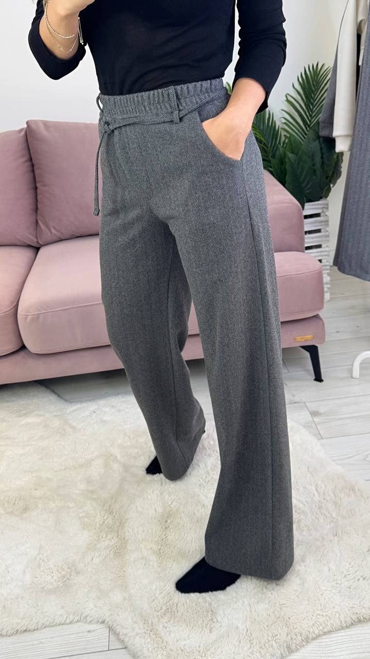 Person wearing gray wide-leg pants and a black top in a living room setting.