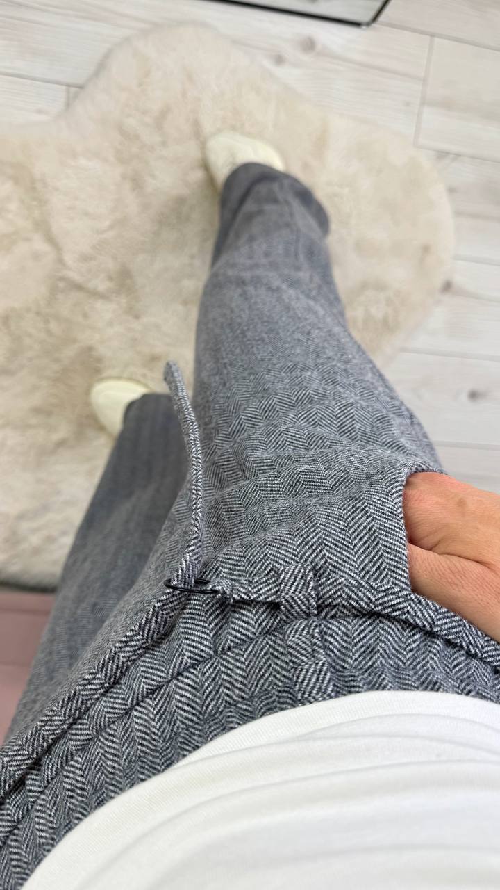 Person wearing gray pants and white shoes on a light wooden floor.