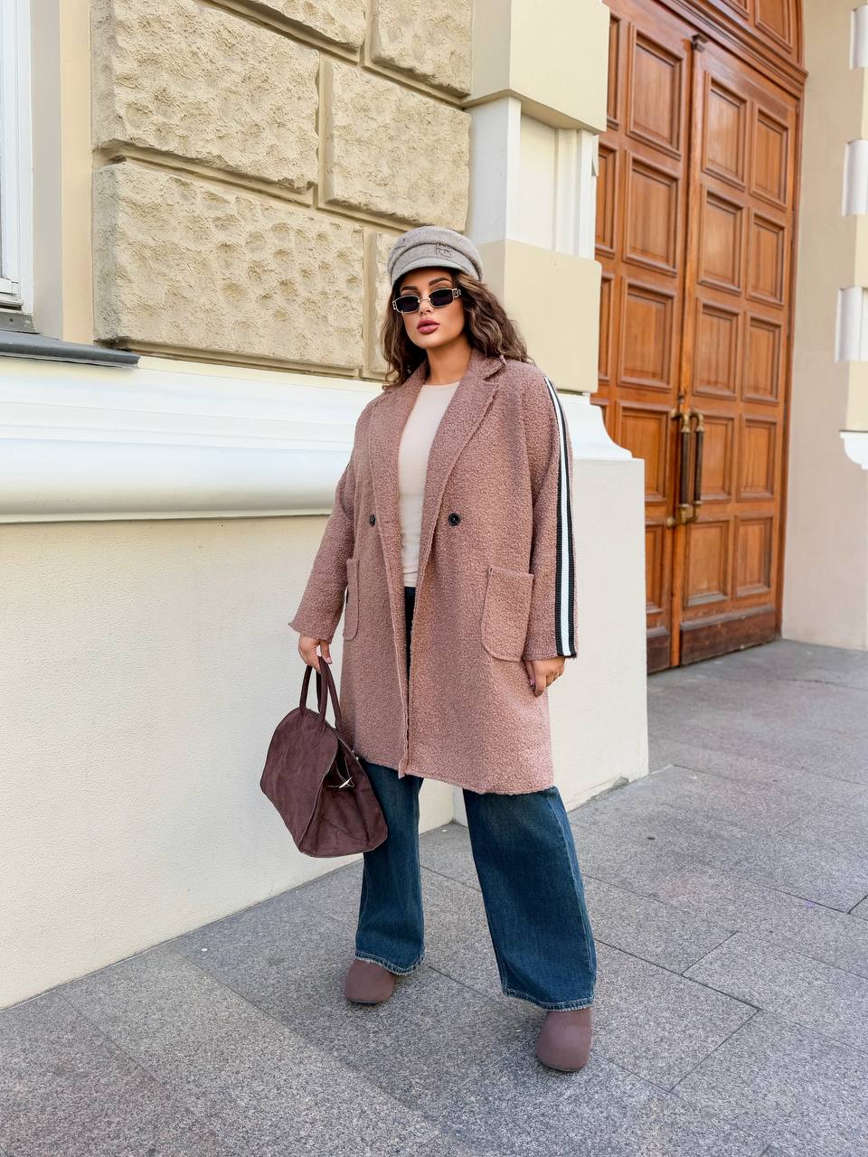 Woman in a long pink coat standing on a sidewalk with a building in the background