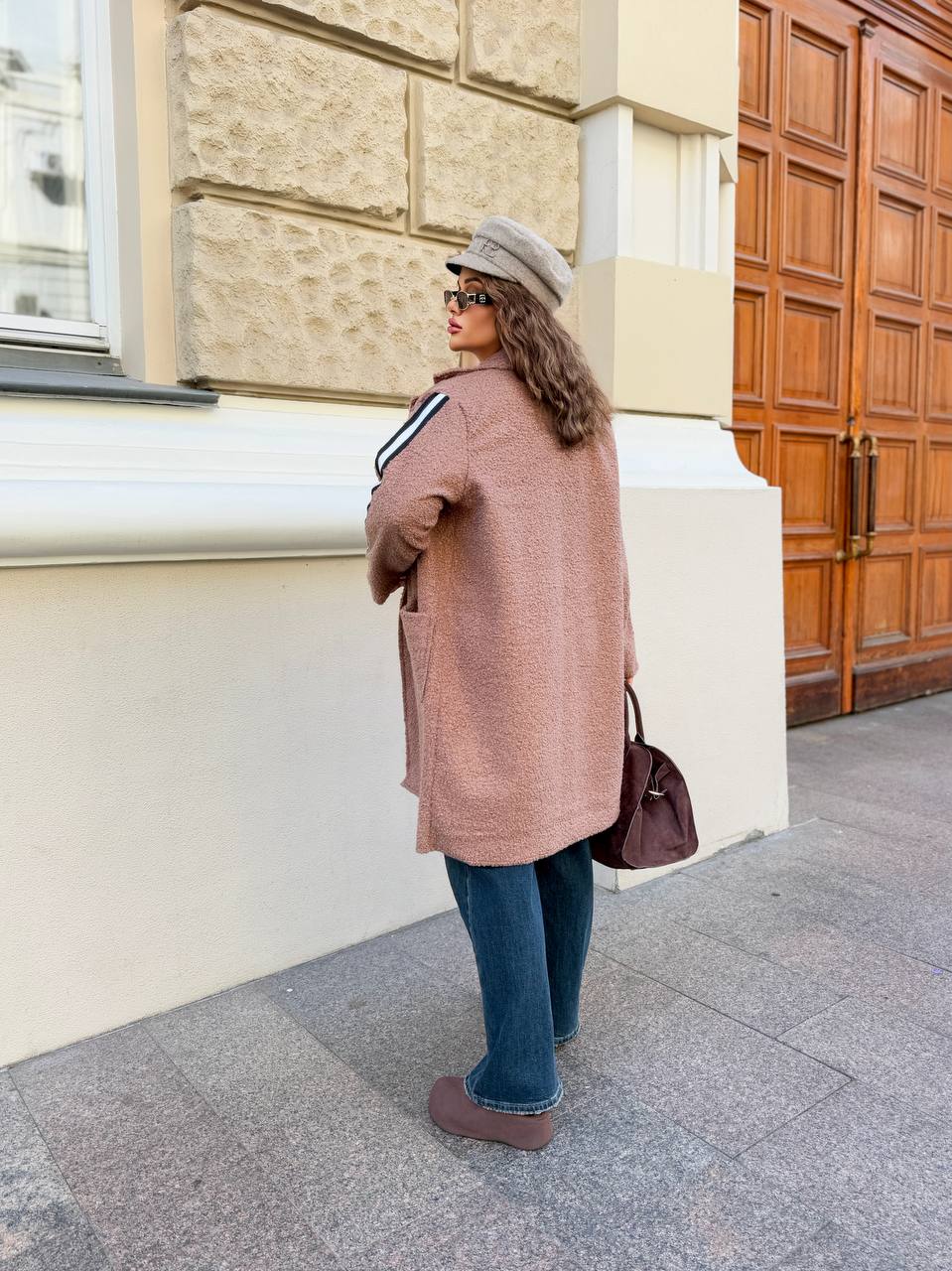 Woman in a long coat and hat standing on a street with a building in the background