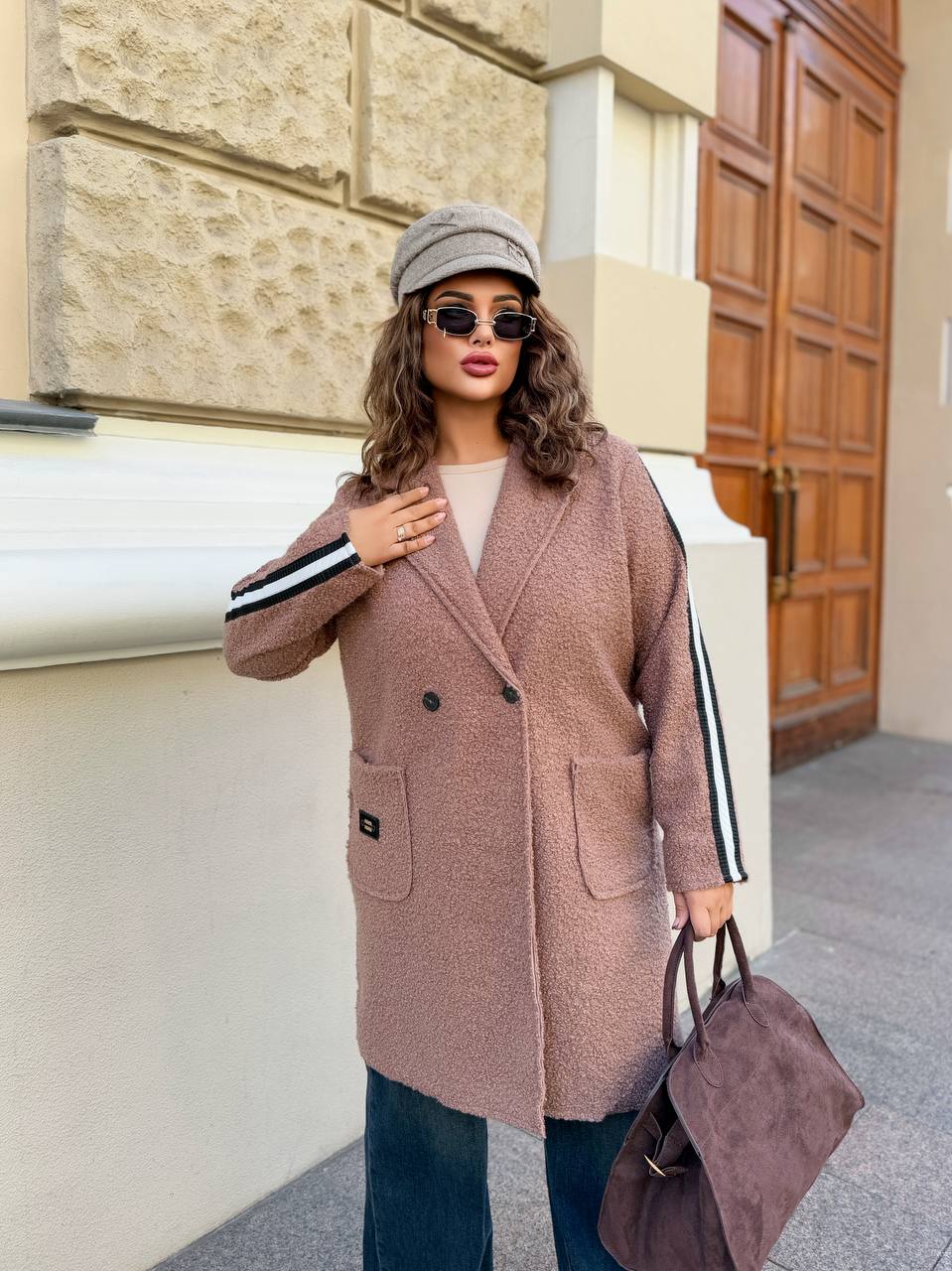 Woman wearing a long pink coat and sunglasses, standing in front of a building.