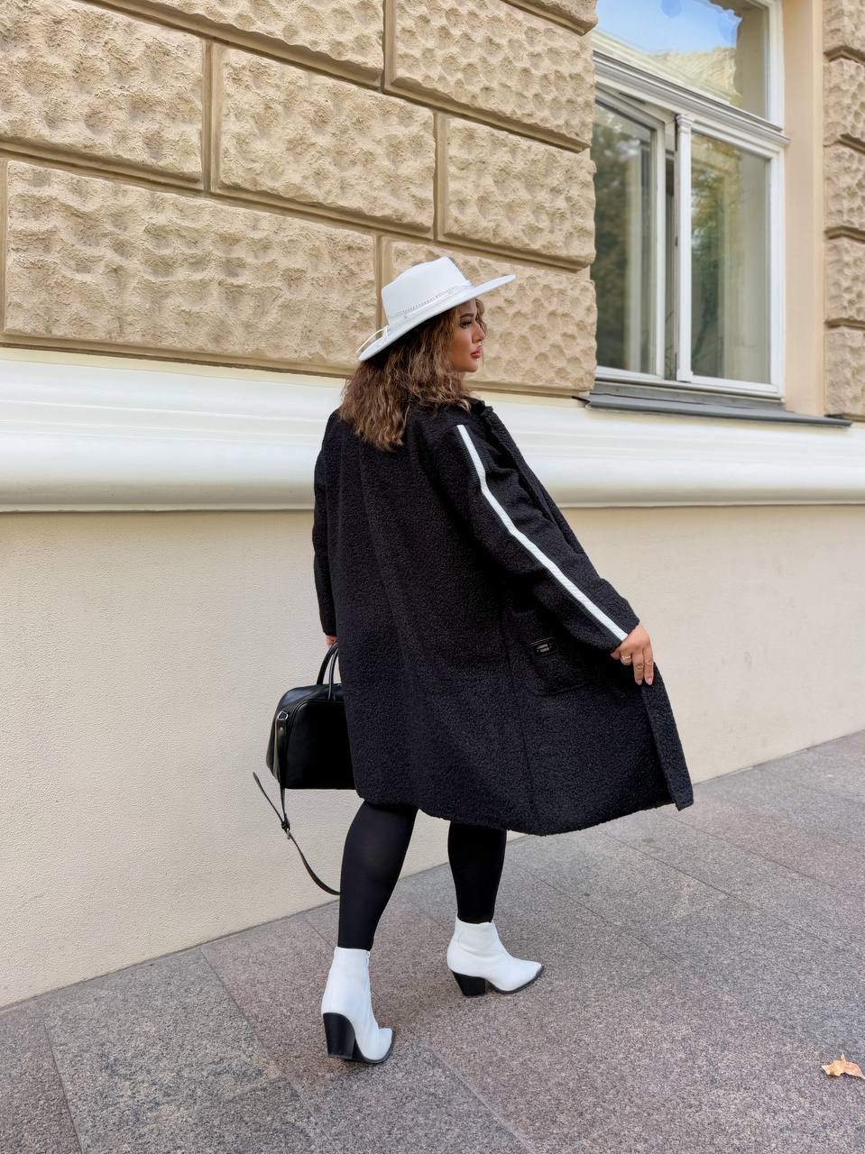Woman in a black coat and white hat standing in front of a building