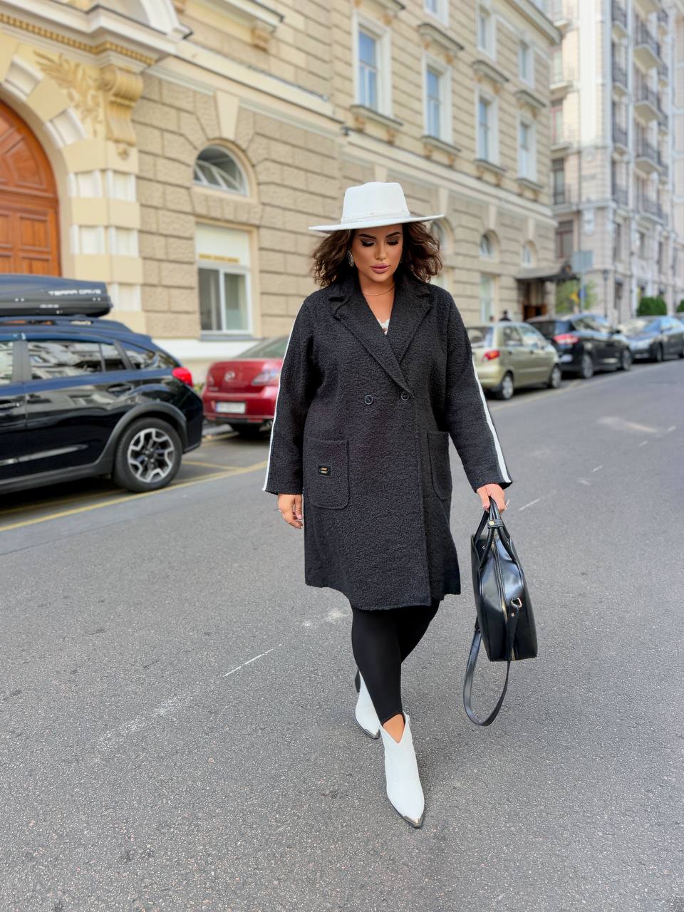 Woman walking on a city street wearing a black coat and white shoes.