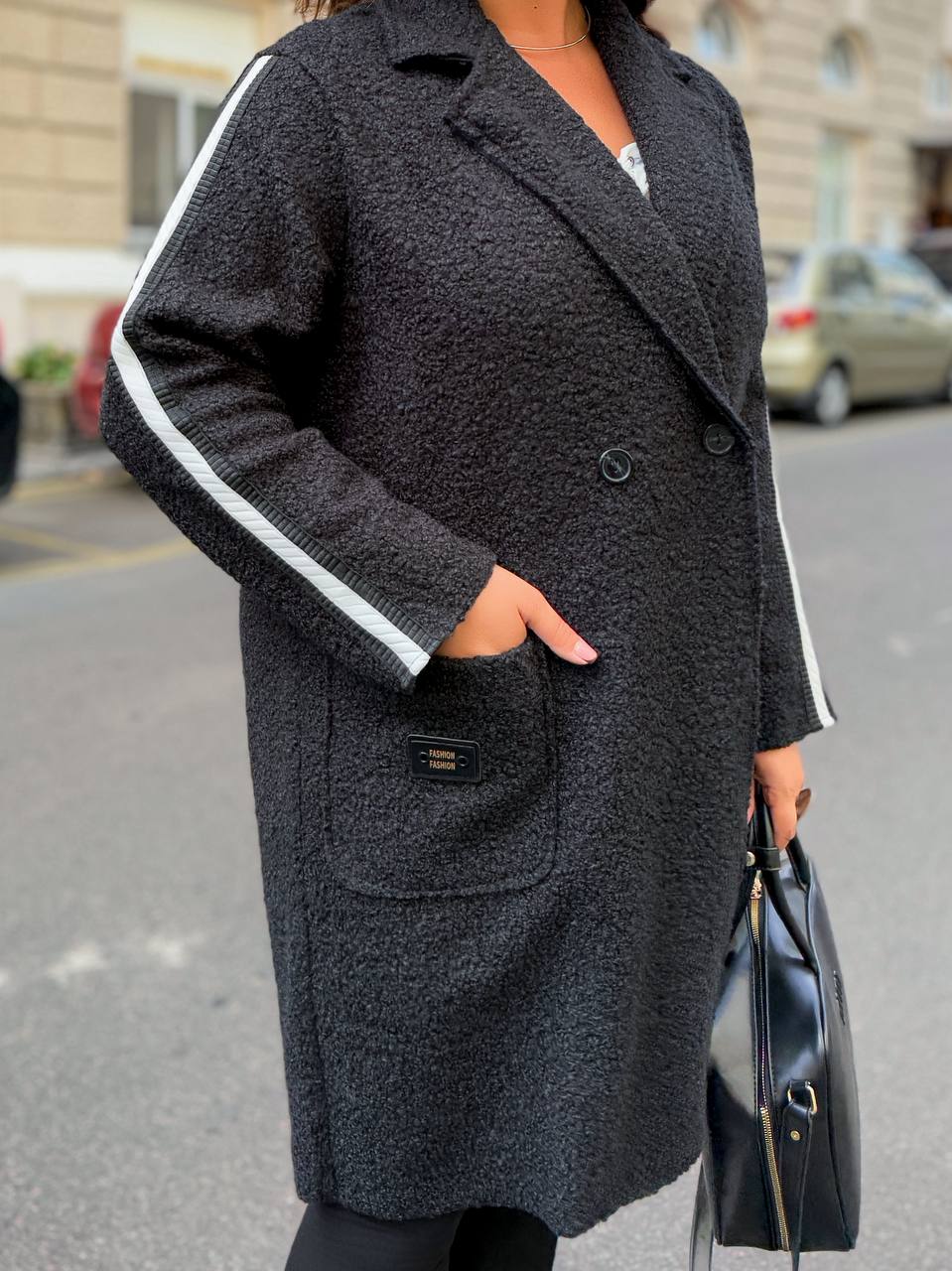 Person wearing a dark gray coat with white trim on a street.