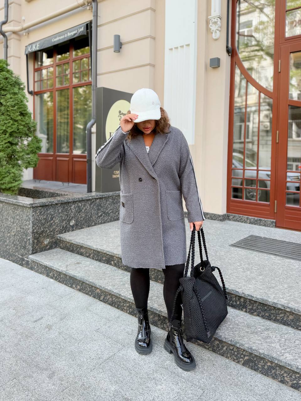 Person wearing a gray coat and black shoes standing on steps outside a building.